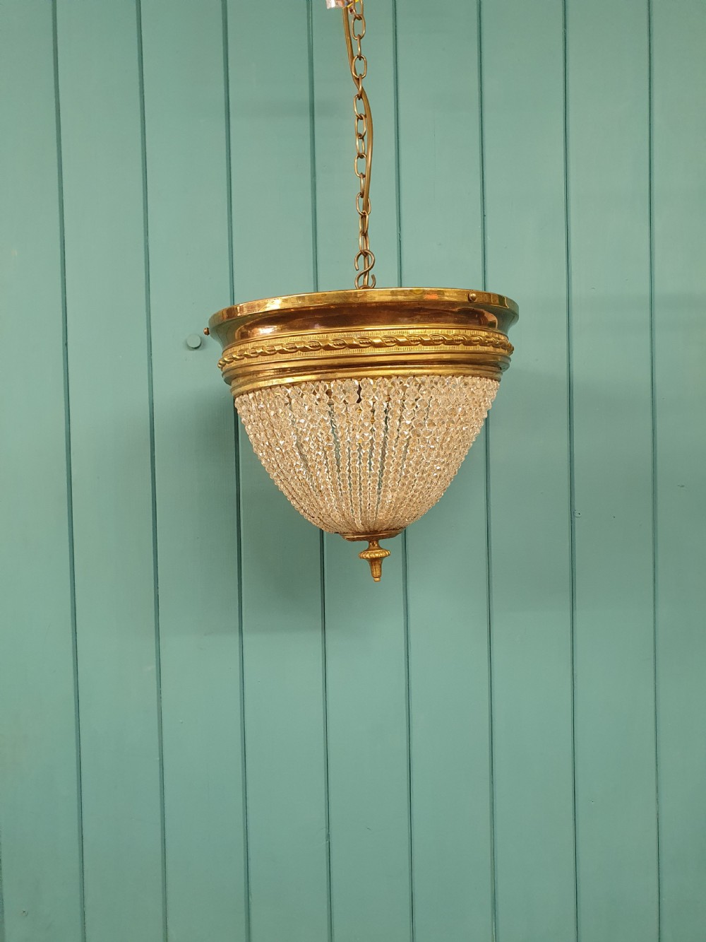 An early 20th-century ceiling light featuring a circular brass band with twisted detail above cascading strands of clear cut glass beads terminating at a brass finial. View VII