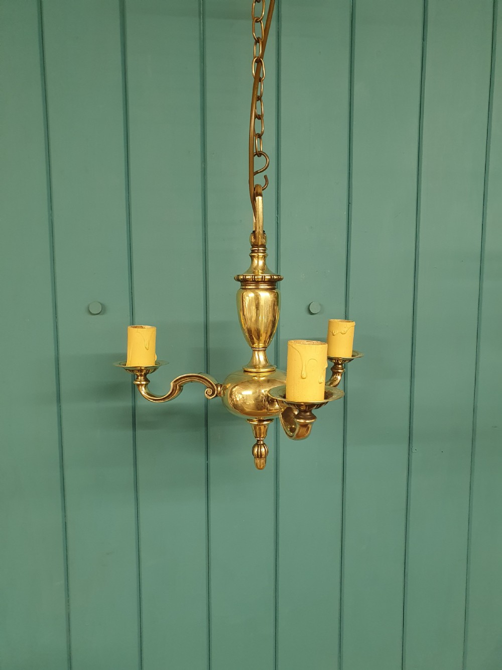 An early 20th-century three-arm brass chandelier featuring a central baluster stem, curved branches, faux candle sleeves, and a hanging chain.
