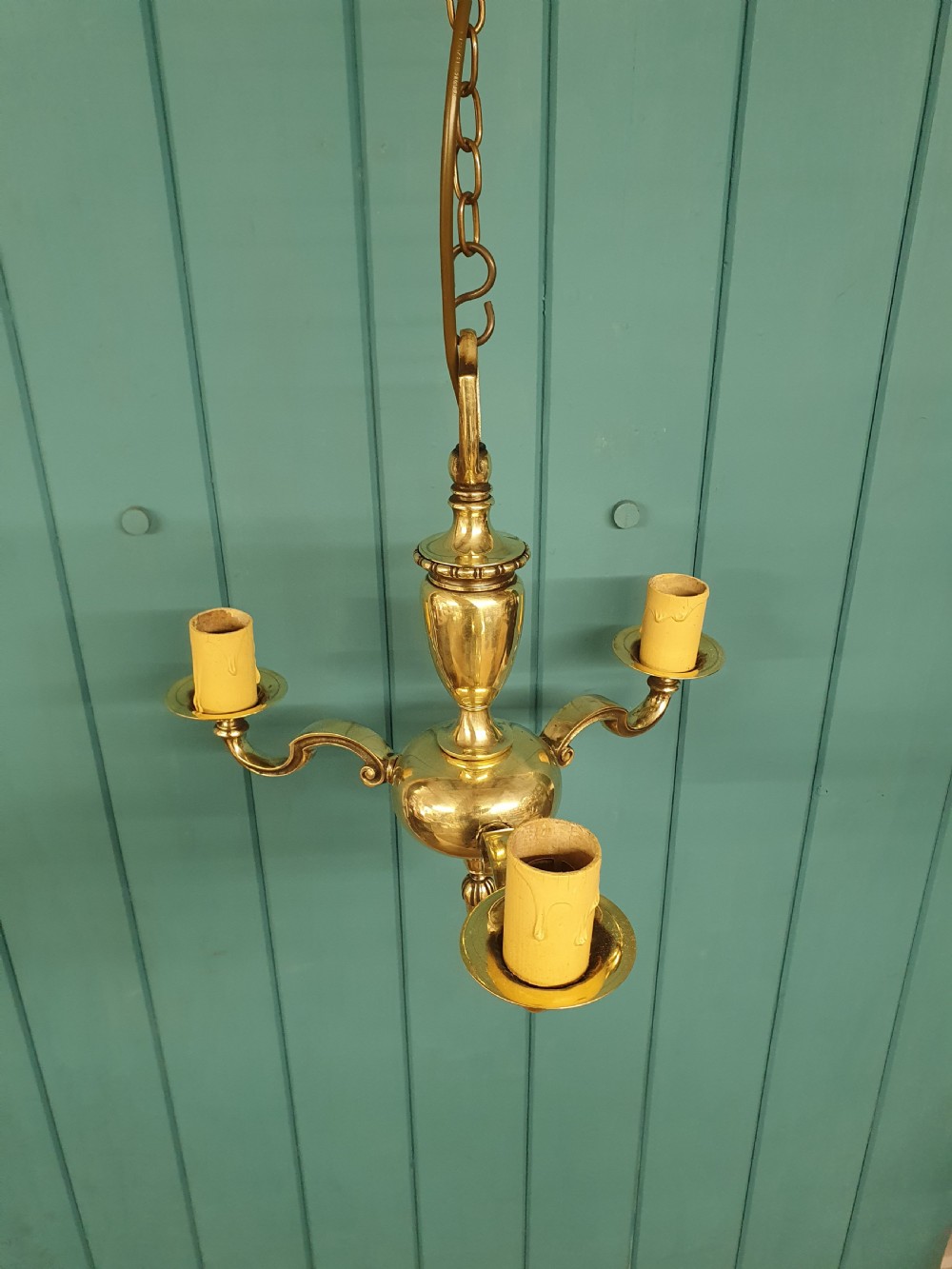 An early 20th-century three-arm brass chandelier featuring a central baluster stem, curved branches, faux candle sleeves, and a hanging chain. View II