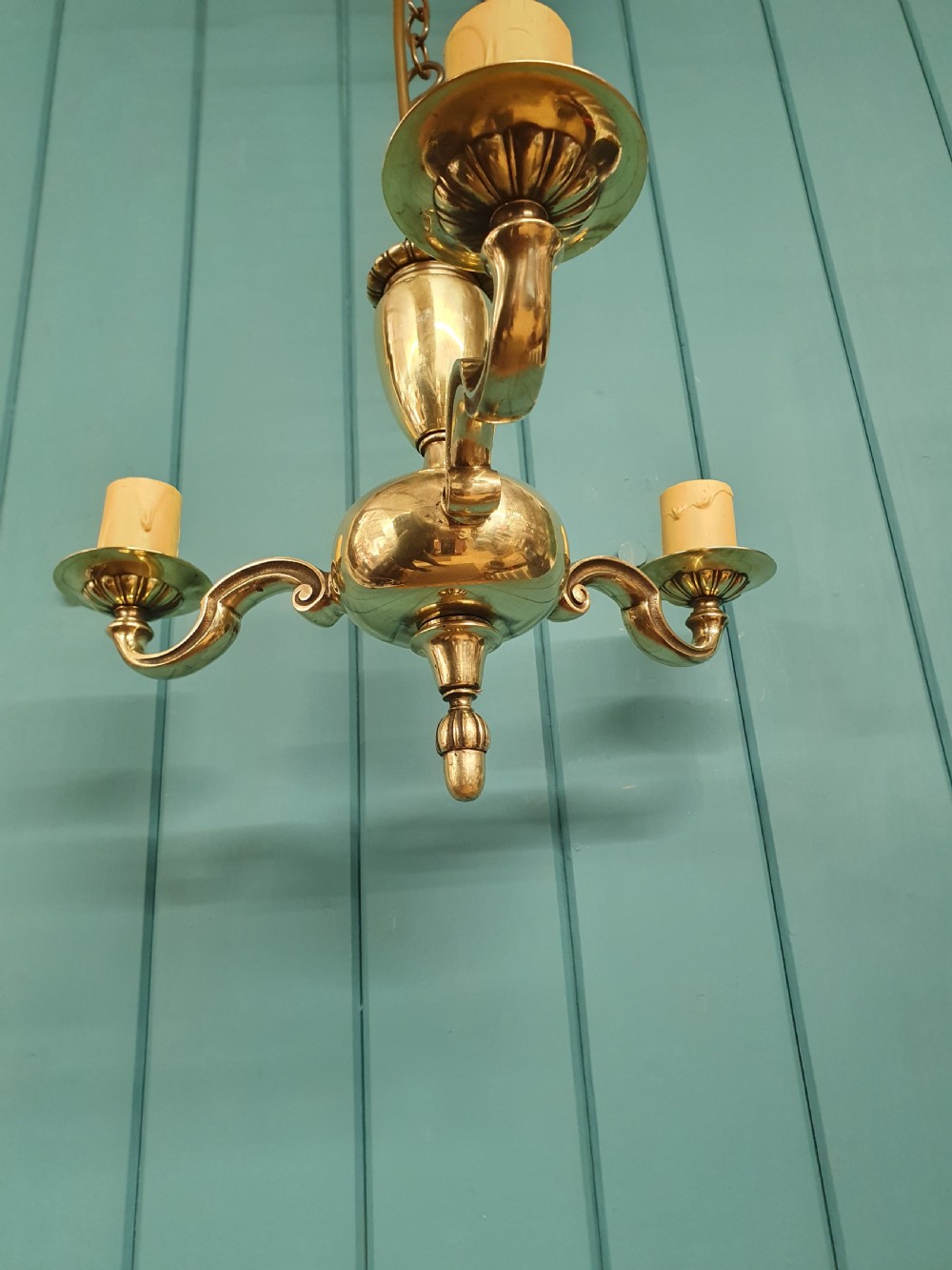 An early 20th-century three-arm brass chandelier featuring a central baluster stem, curved branches, faux candle sleeves, and a hanging chain. View III