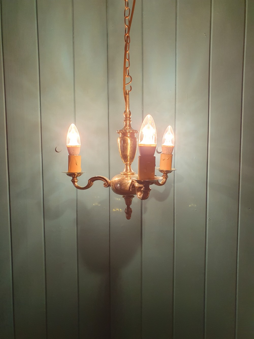 An early 20th-century three-arm brass chandelier featuring a central baluster stem, curved branches, faux candle sleeves, and a hanging chain. View VI