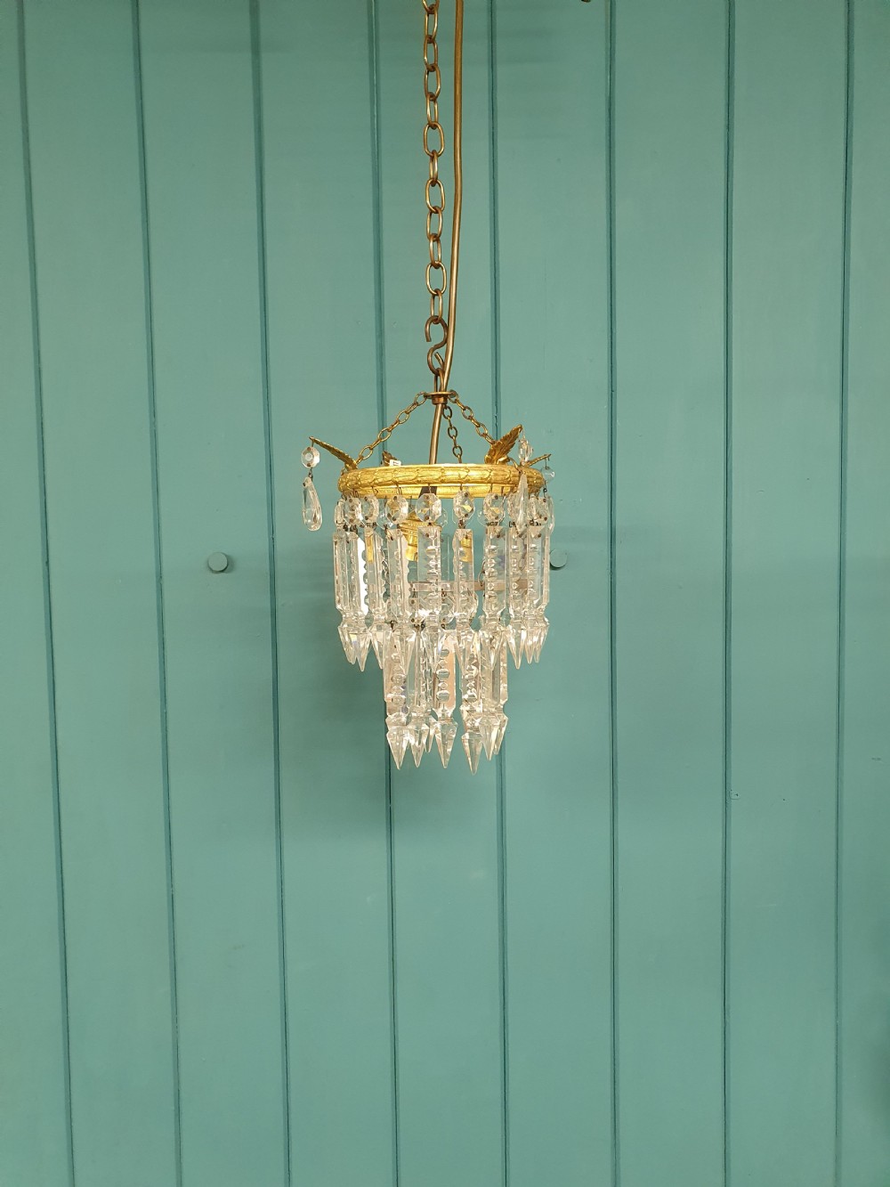 An early 20th-century ceiling chandelier featuring a circular brass ring adorned with tiered hanging clear crystal prisms suspended from a chain.