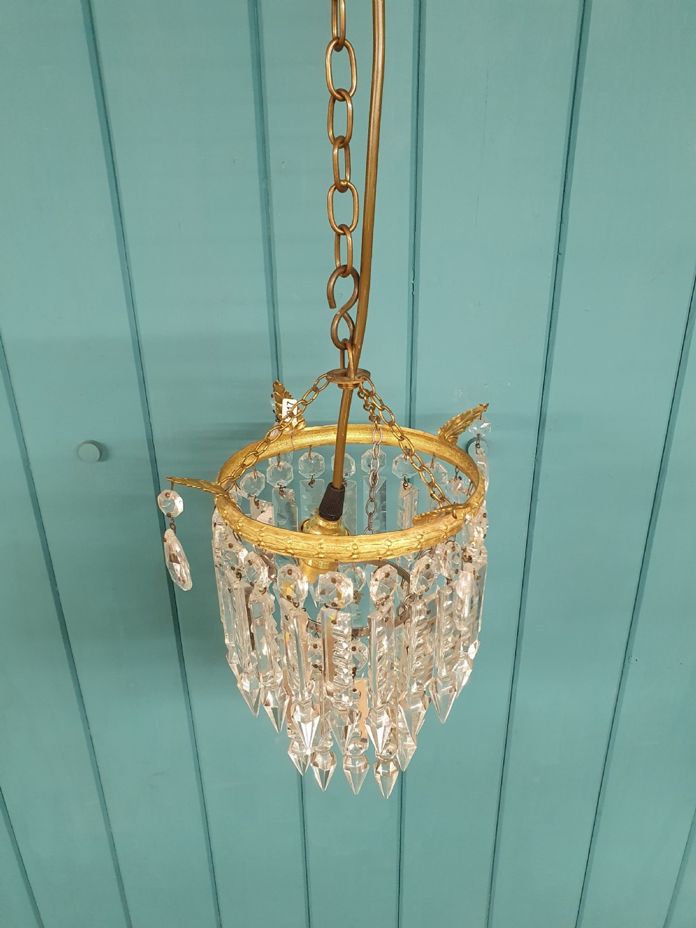 An early 20th-century ceiling chandelier featuring a circular brass ring adorned with tiered hanging clear crystal prisms suspended from a chain. View II