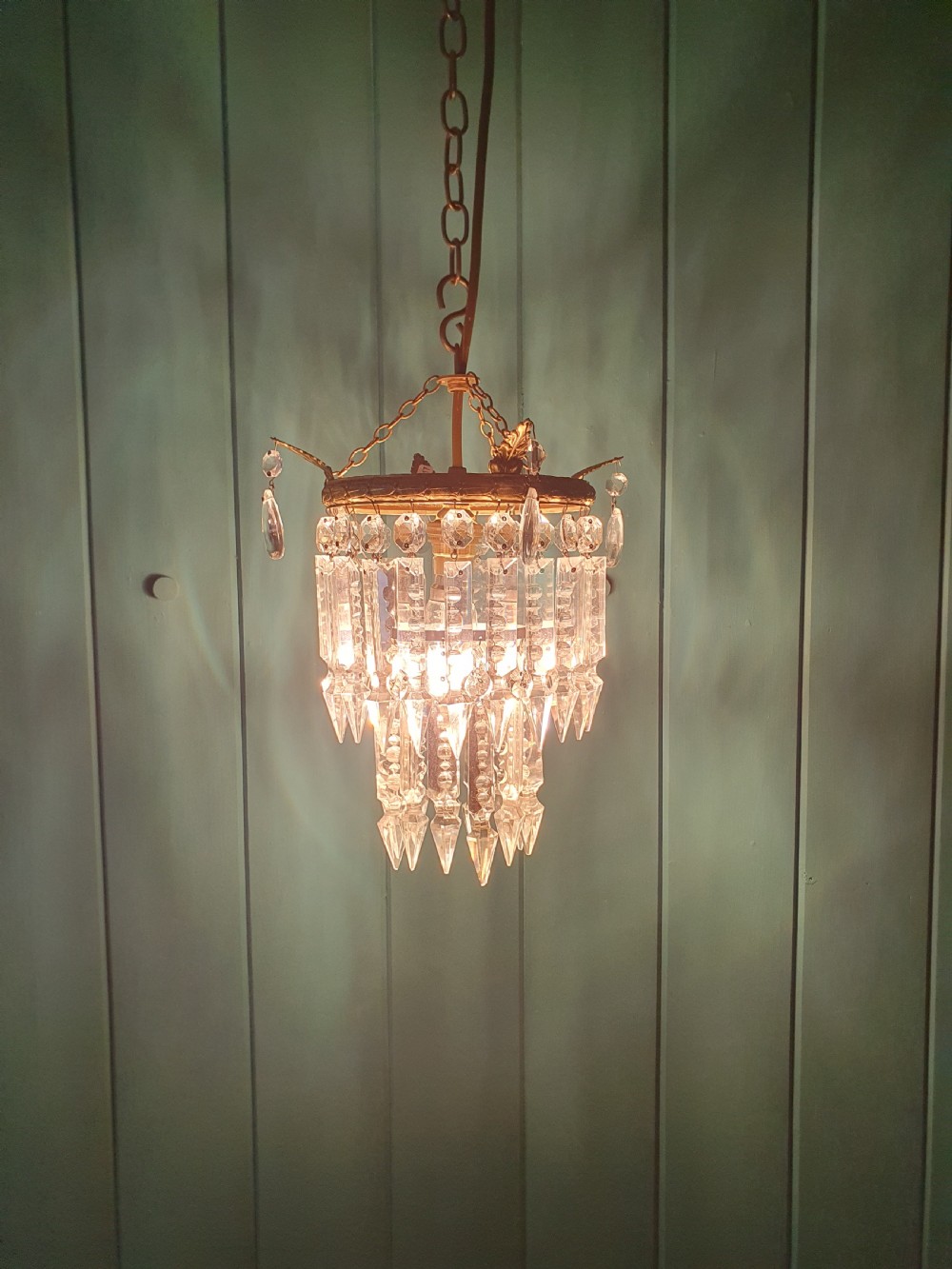 An early 20th-century ceiling chandelier featuring a circular brass ring adorned with tiered hanging clear crystal prisms suspended from a chain. View IV