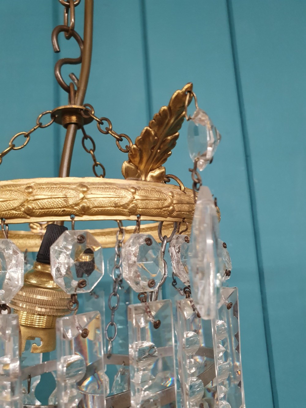 An early 20th-century ceiling chandelier featuring a circular brass ring adorned with tiered hanging clear crystal prisms suspended from a chain. View V