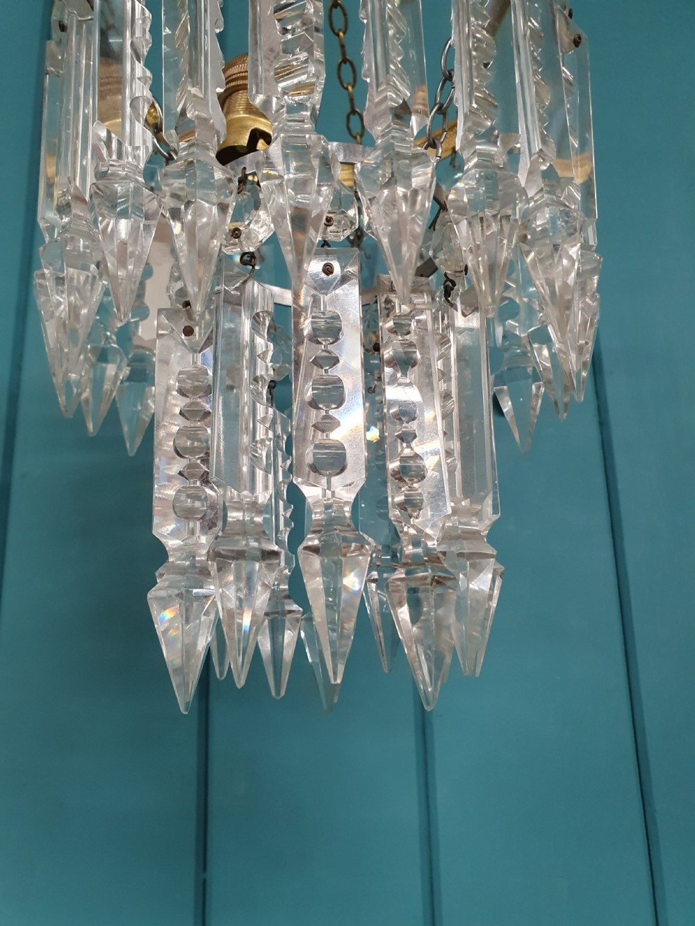 An early 20th-century ceiling chandelier featuring a circular brass ring adorned with tiered hanging clear crystal prisms suspended from a chain. View VI