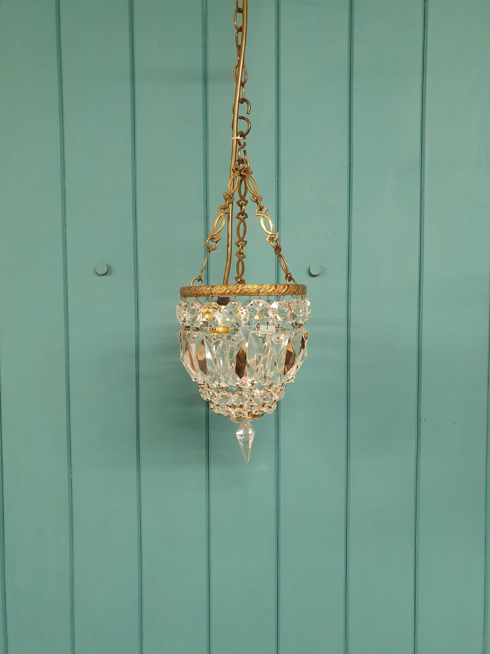 An antique crystal bag chandelier featuring tiered glass prisms suspended from a stamped brass frame and suspension chain.