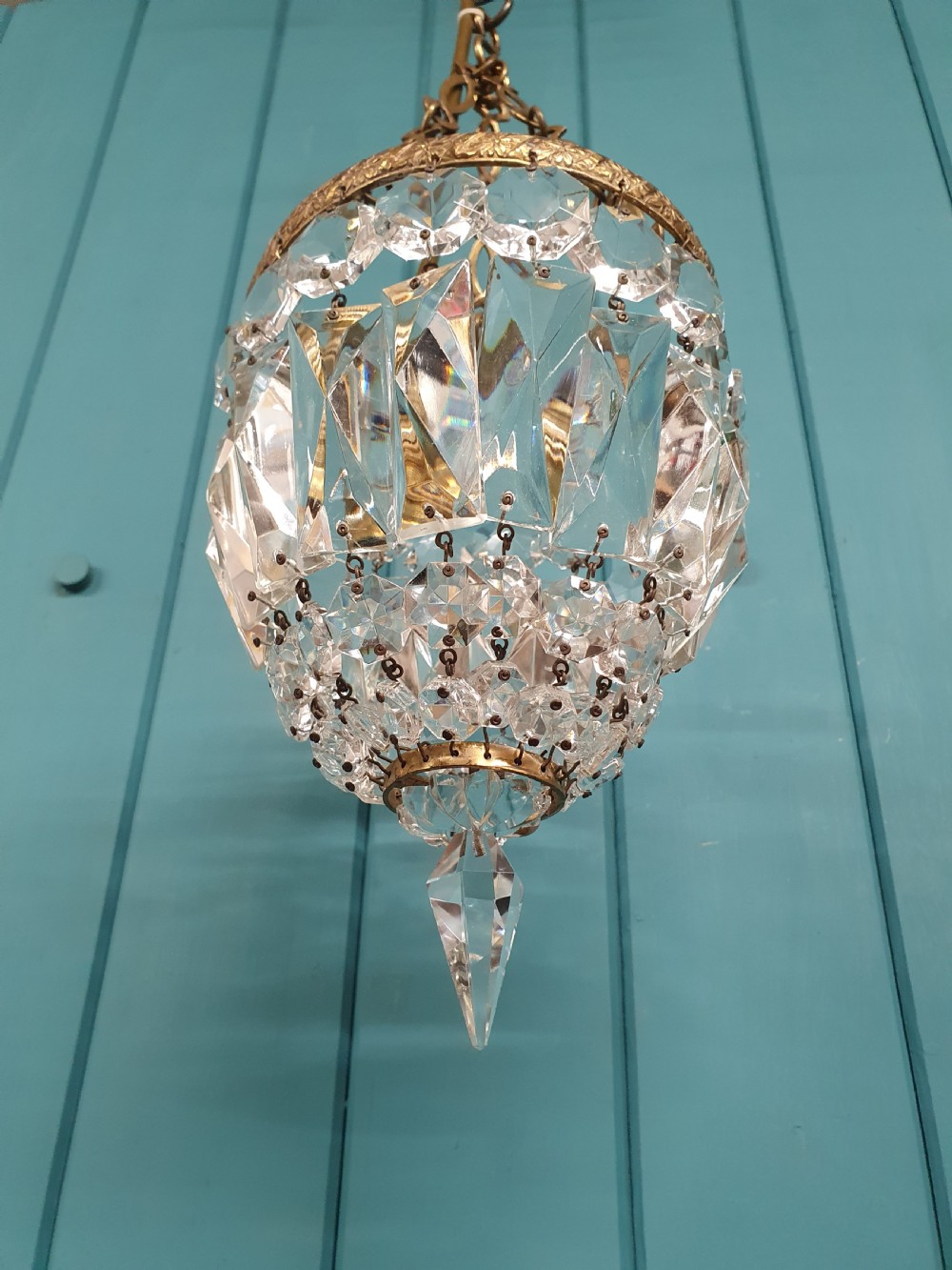 An antique crystal bag chandelier featuring tiered glass prisms suspended from a stamped brass frame and suspension chain. View II