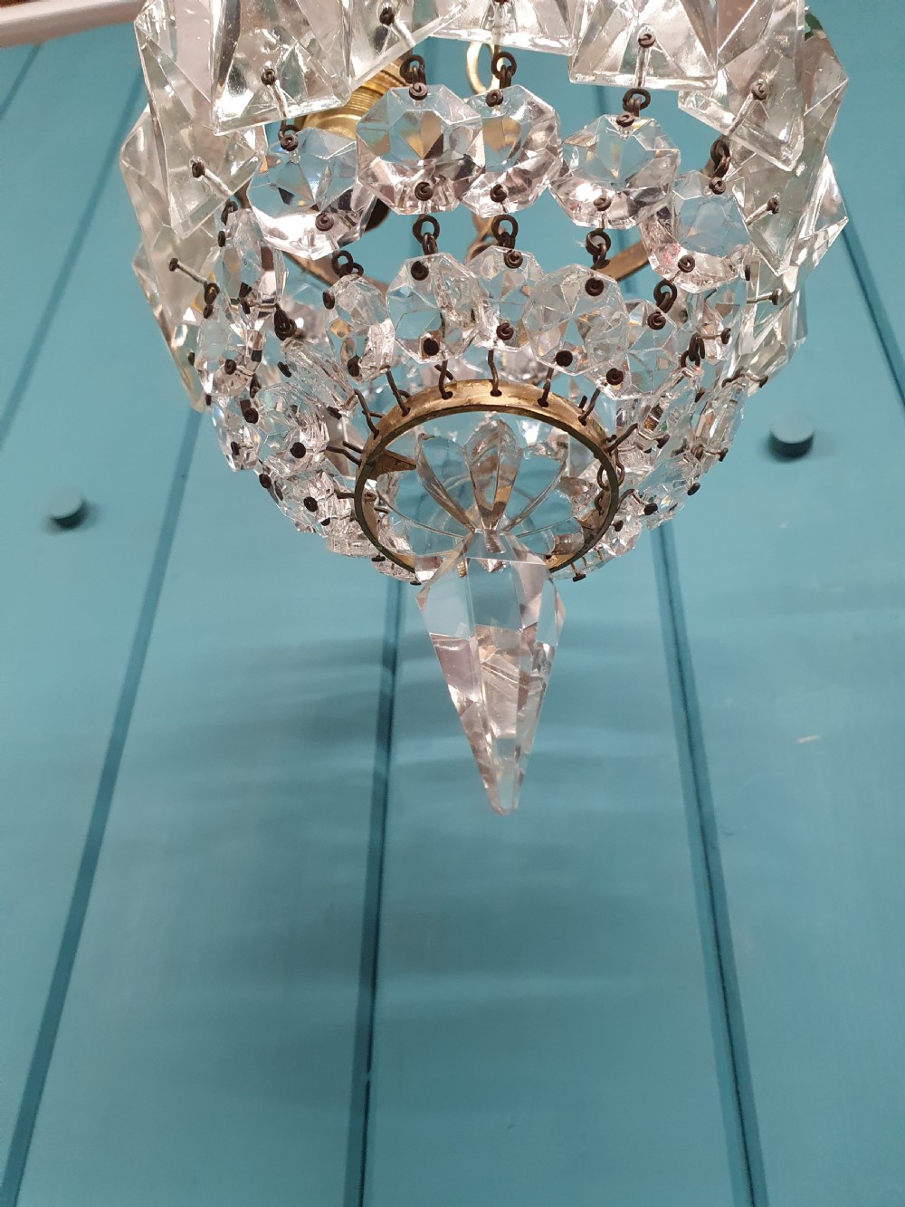 An antique crystal bag chandelier featuring tiered glass prisms suspended from a stamped brass frame and suspension chain. View III