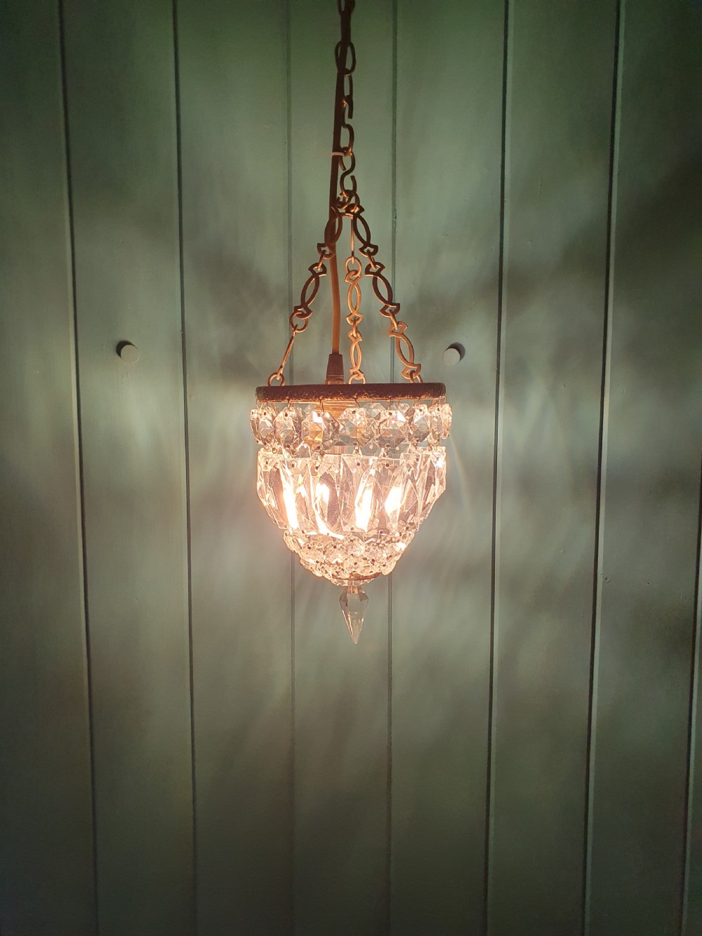 An antique crystal bag chandelier featuring tiered glass prisms suspended from a stamped brass frame and suspension chain. View IV