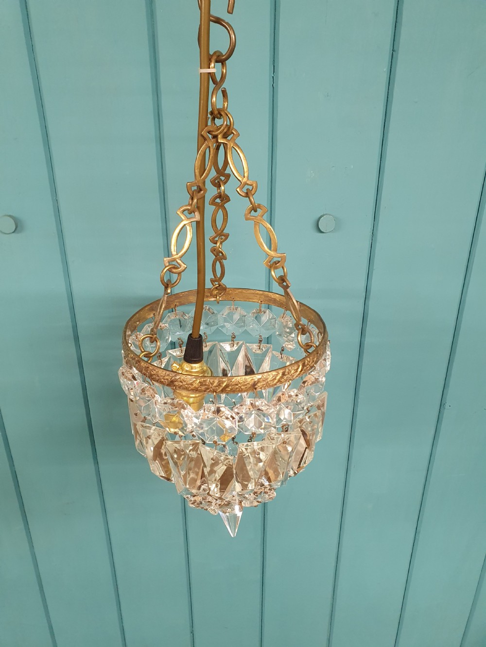 An antique crystal bag chandelier featuring tiered glass prisms suspended from a stamped brass frame and suspension chain. View V