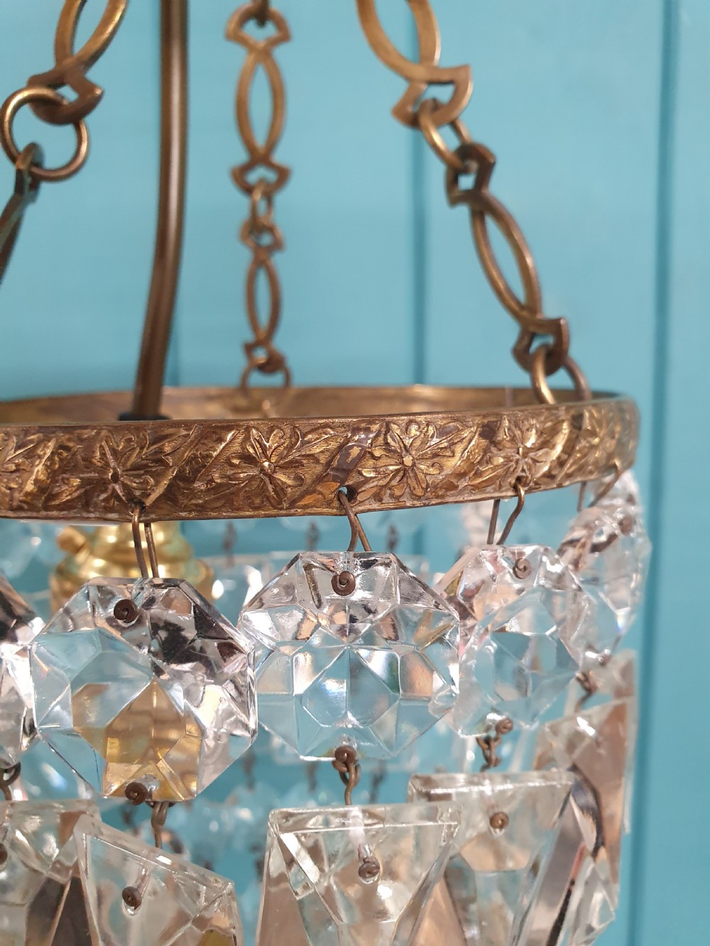 An antique crystal bag chandelier featuring tiered glass prisms suspended from a stamped brass frame and suspension chain. View VI