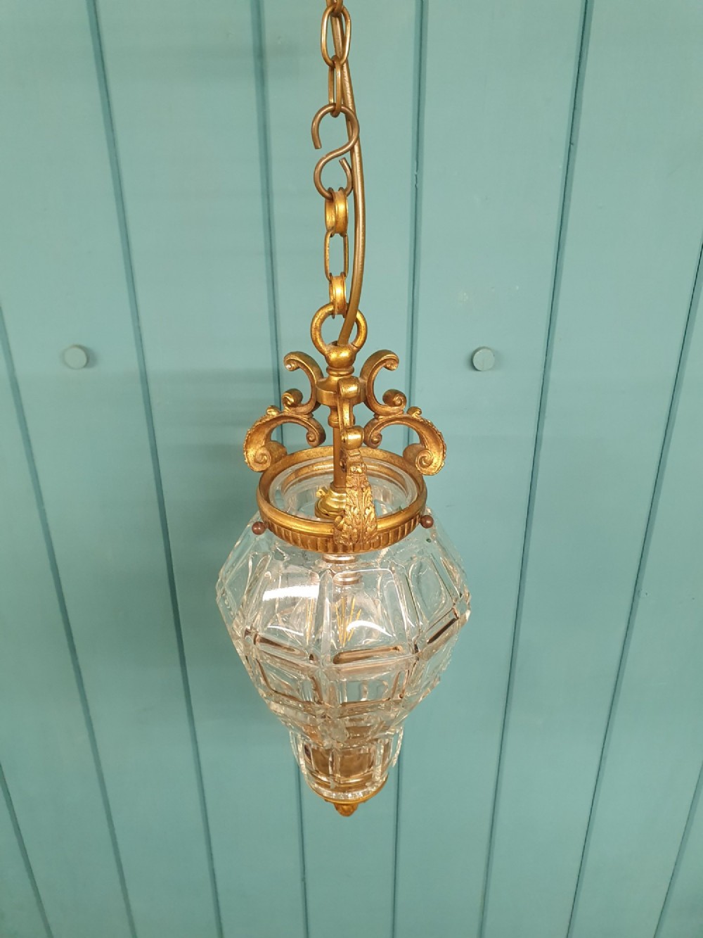 A French brass pendant lantern featuring a faceted moulded glass shade, ornate brass scroll crown, and suspension chain. View III