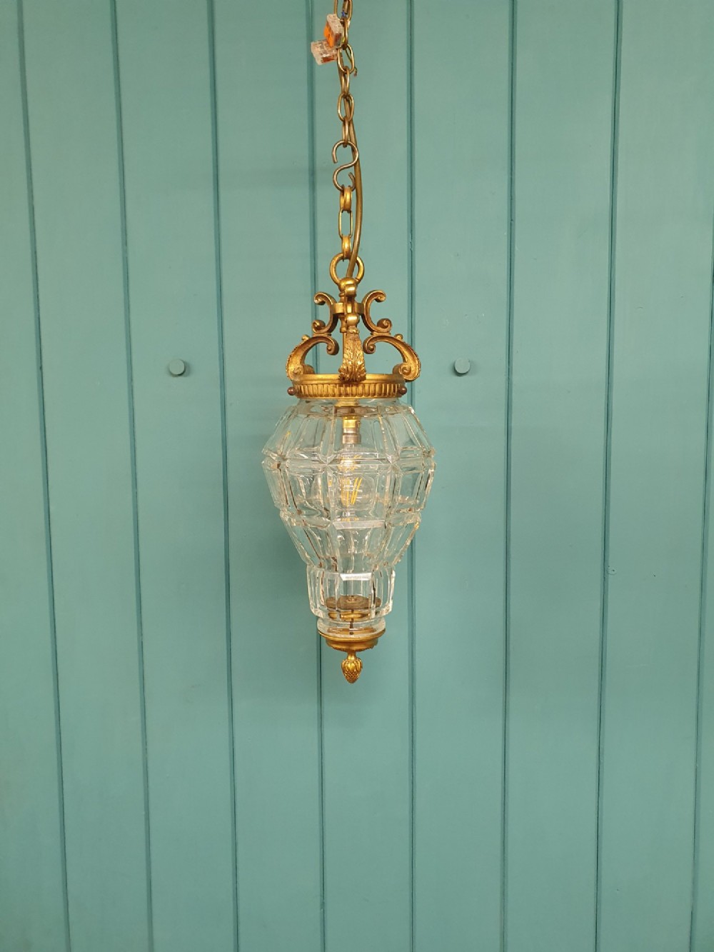 A French brass pendant lantern featuring a faceted moulded glass shade, ornate brass scroll crown, and suspension chain. View IV