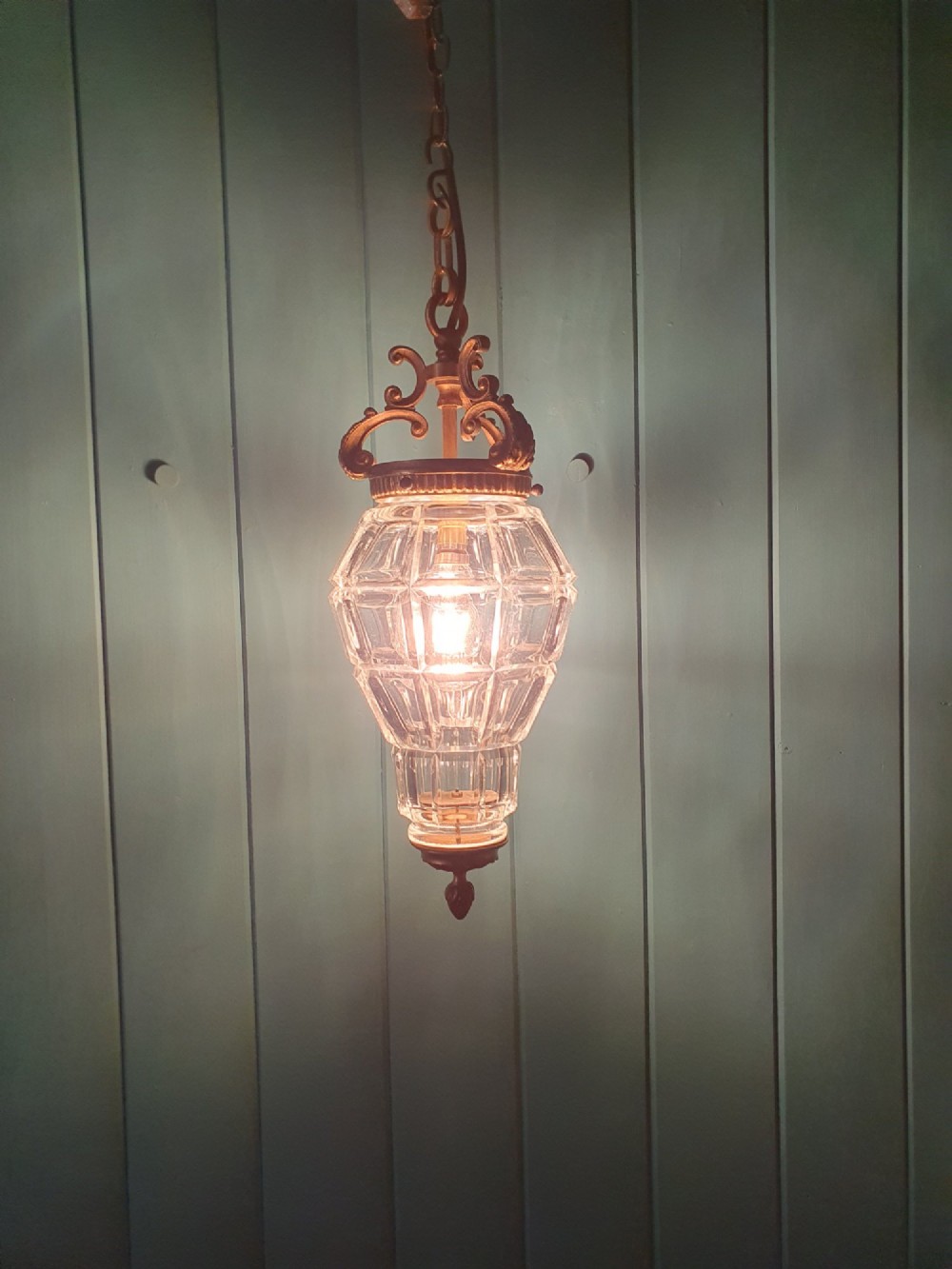 A French brass pendant lantern featuring a faceted moulded glass shade, ornate brass scroll crown, and suspension chain. View V