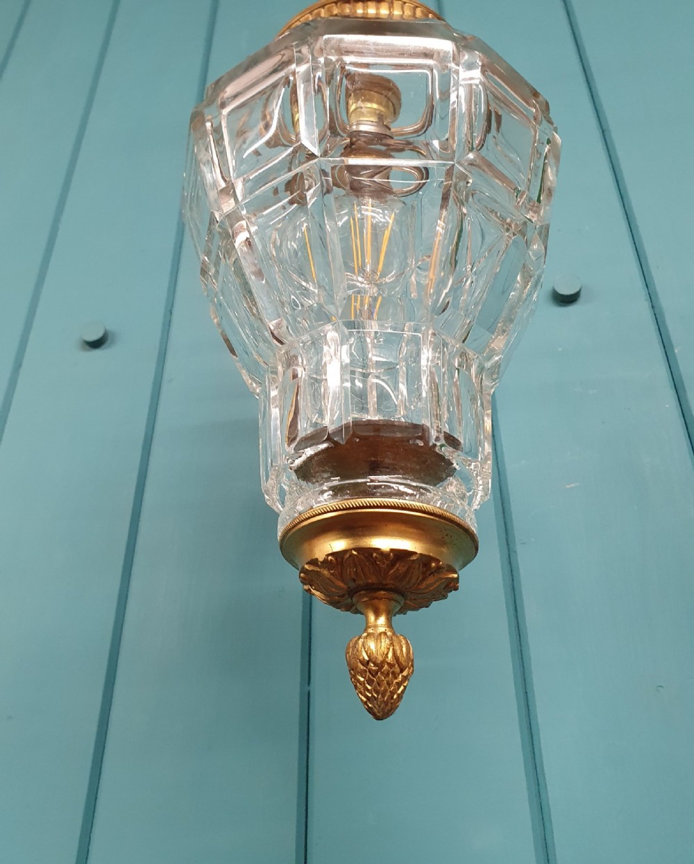 A French brass pendant lantern featuring a faceted moulded glass shade, ornate brass scroll crown, and suspension chain. View VI