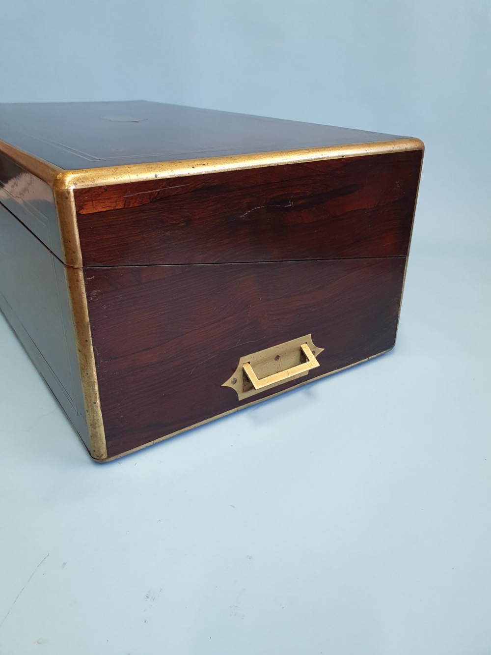 A rectangular dark rosewood writing slope featuring brass inlay stringing, brass corner brackets, a keyhole, and a central brass cartouche. View IV