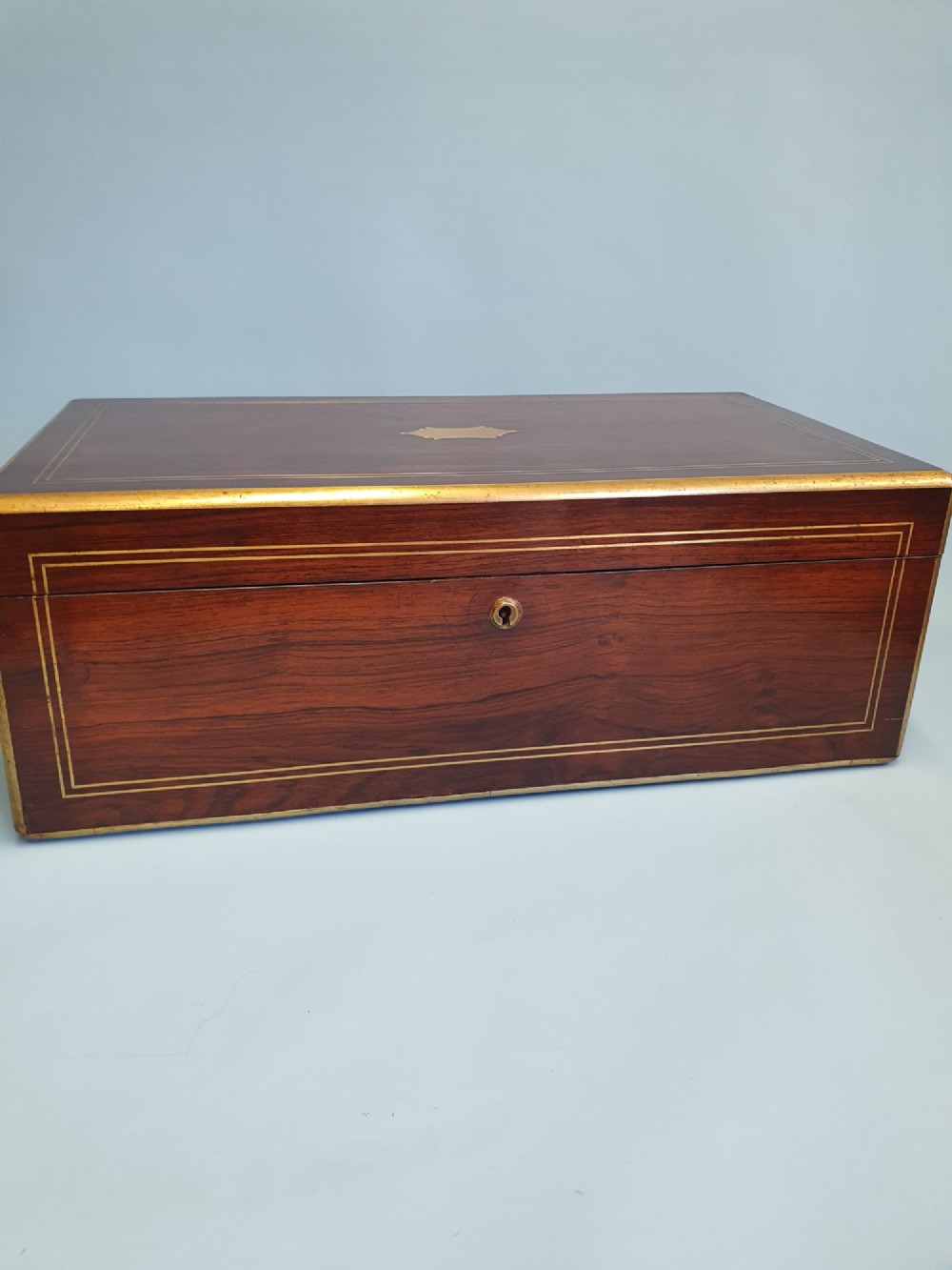 A rectangular dark rosewood writing slope featuring brass inlay stringing, brass corner brackets, a keyhole, and a central brass cartouche. View VI