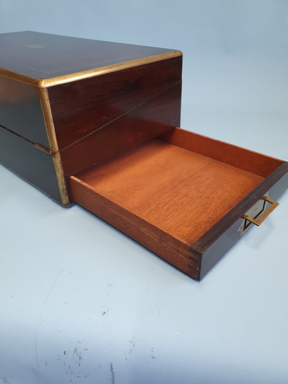 A rectangular dark rosewood writing slope featuring brass inlay stringing, brass corner brackets, a keyhole, and a central brass cartouche. View VII