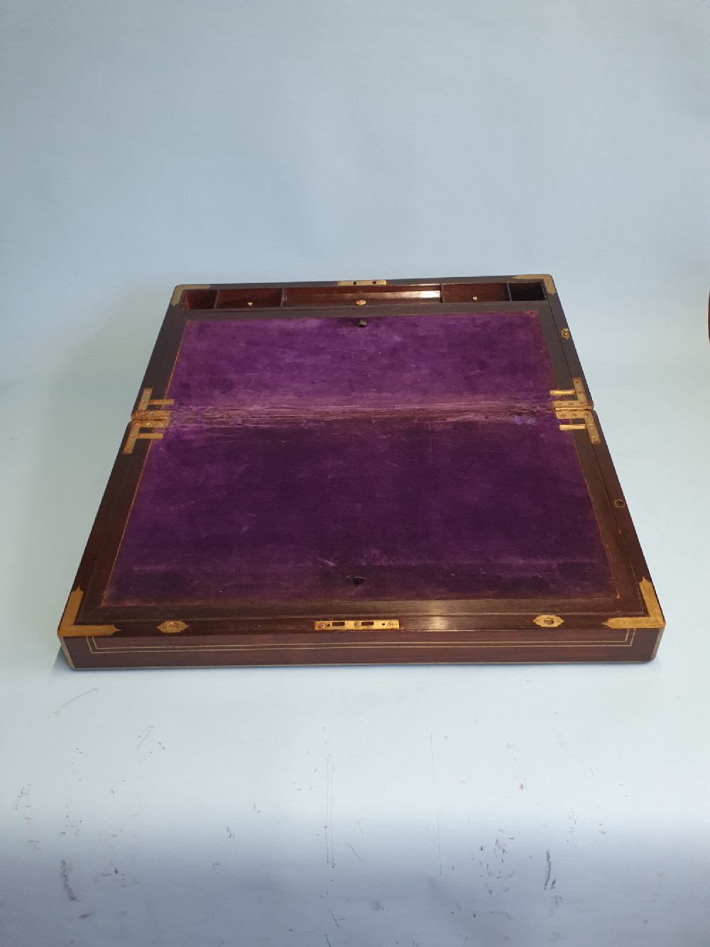 A rectangular dark rosewood writing slope featuring brass inlay stringing, brass corner brackets, a keyhole, and a central brass cartouche. View IX
