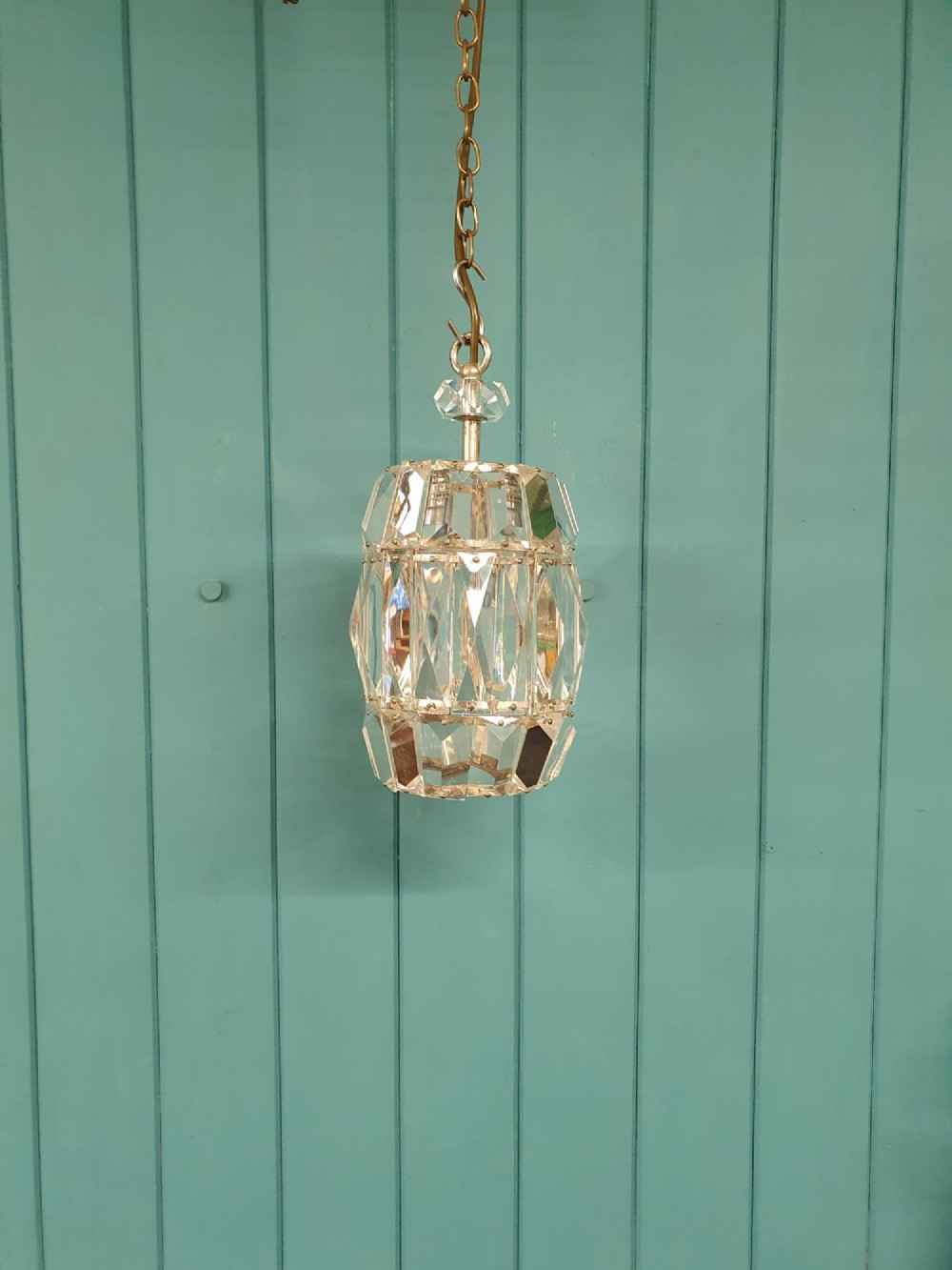 An early 20th-century small barrel-shaped crystal prism chandelier suspended by a brass link chain.