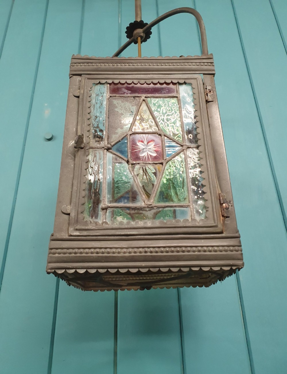 A Victorian hall lantern featuring a rectangular metal frame, an arched suspension handle, and leaded stained glass panels in green, red, and blue geometric patterns. View III