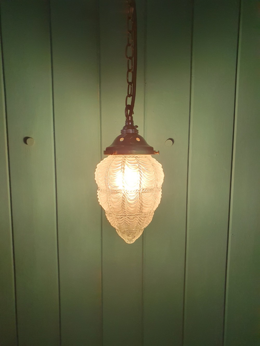 An antique moulded glass pendant light shade with a swag design hanging from a brass gallery and link chain. View II
