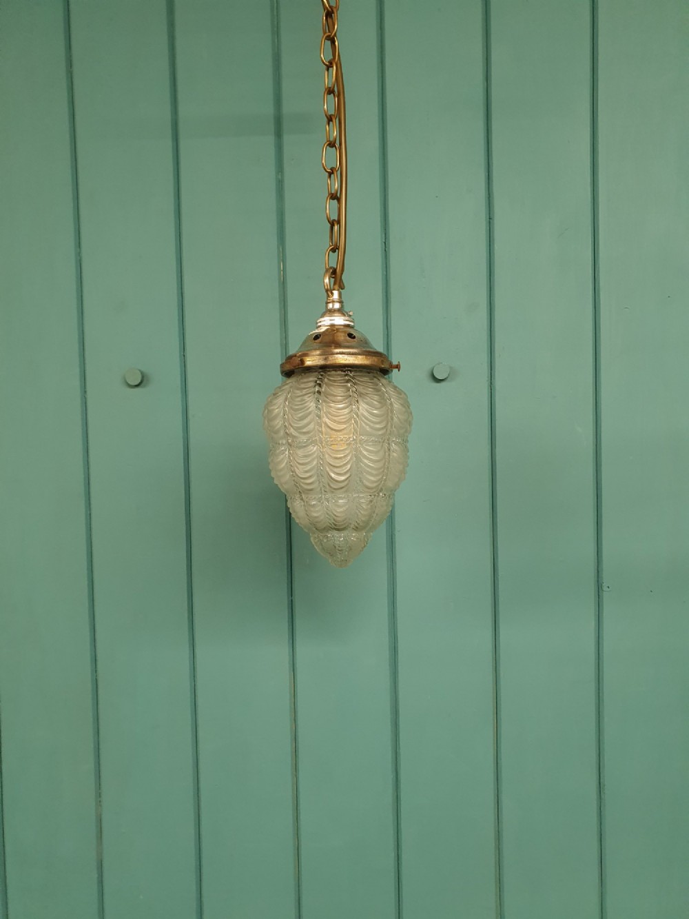 An antique moulded glass pendant light shade with a swag design hanging from a brass gallery and link chain.