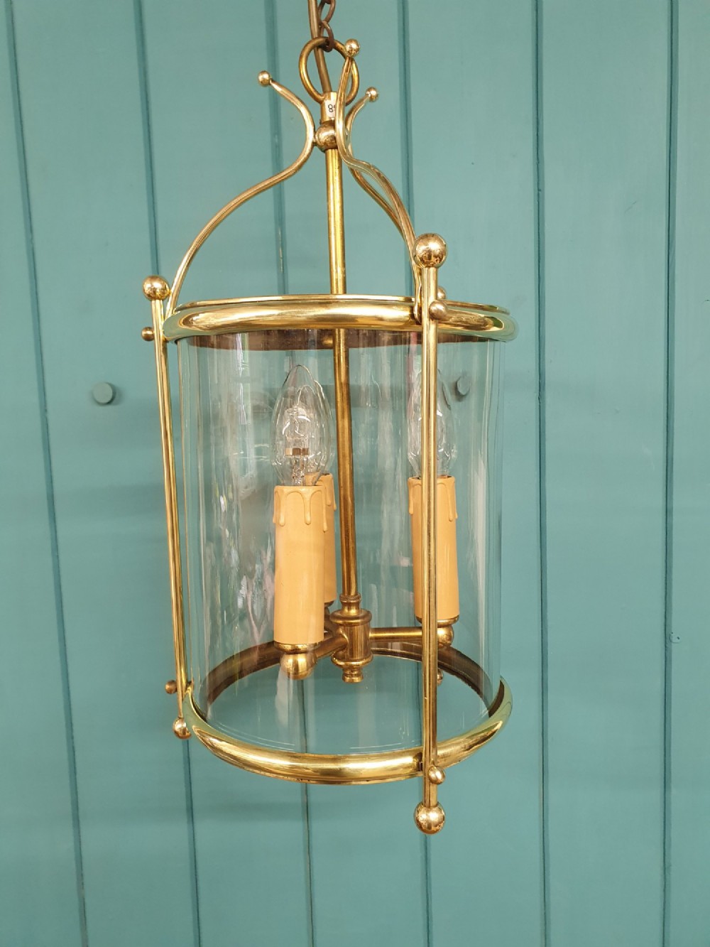 A brass cylindrical hanging hall lantern with clear glass panels, three central candle sleeves, and a suspended brass chain. View II