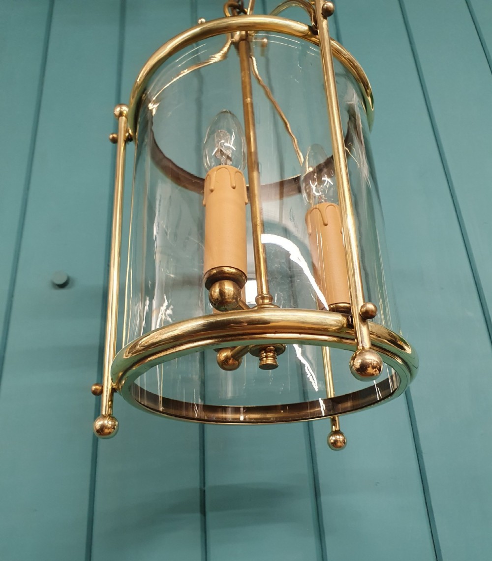 A brass cylindrical hanging hall lantern with clear glass panels, three central candle sleeves, and a suspended brass chain. View IV