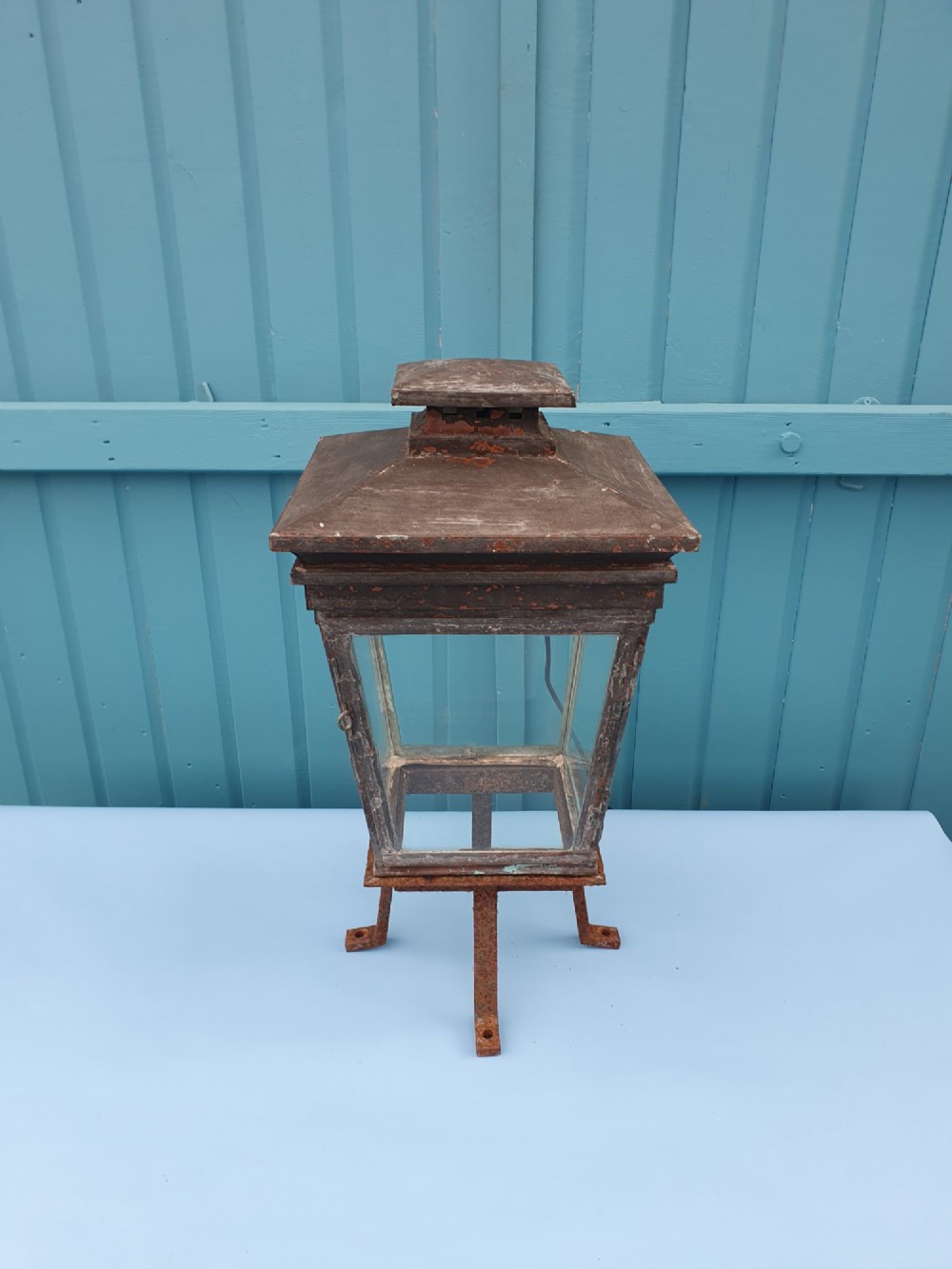 A Victorian weather-worn copper gas lantern converted for electric use, featuring clear glass panels and a stepped pyramidal top cowl supported by an iron mounting base.
