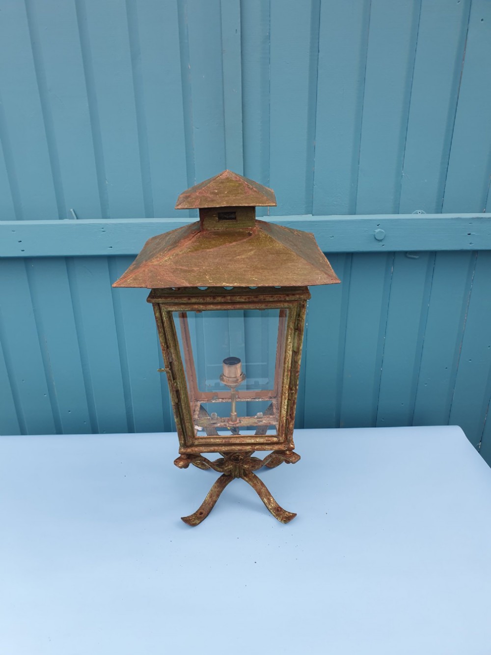 A Victorian green-painted metal garden lantern with glass panes and a tiered top cap, converted for electrical use and mounted on a decorative base.