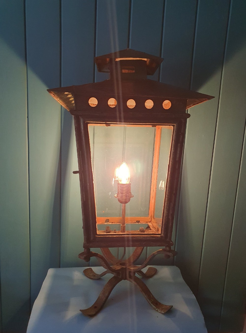 A Victorian green-painted metal garden lantern with glass panes and a tiered top cap, converted for electrical use and mounted on a decorative base. View VII