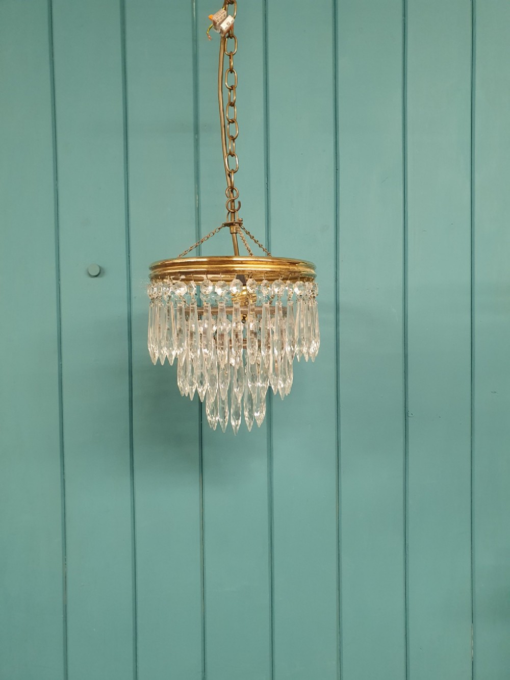 An early 20th-century brass pendant chandelier featuring tiered rings of faceted clear crystal glass spikes suspended from a chain.