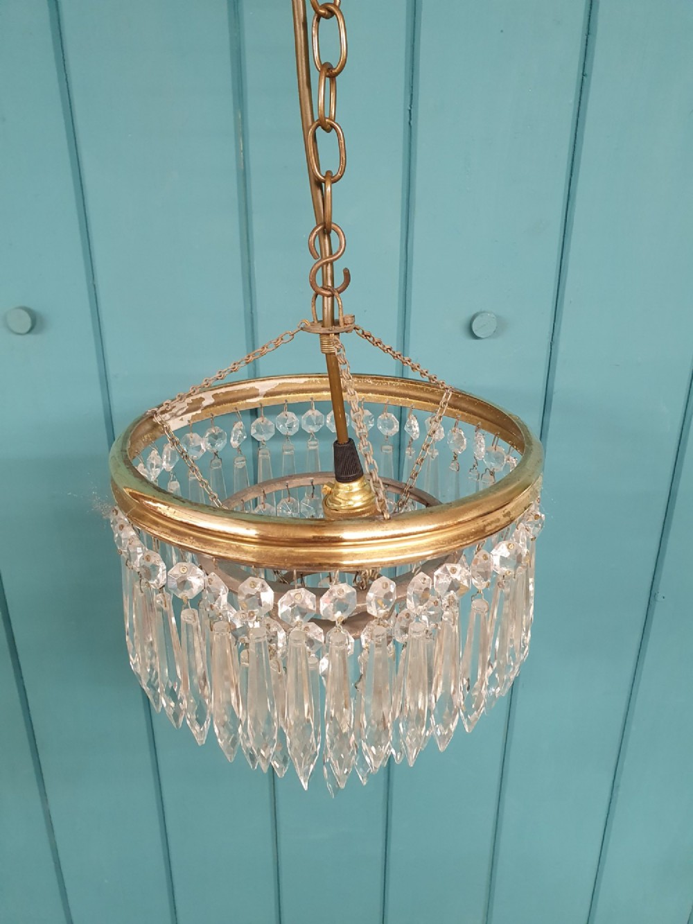 An early 20th-century brass pendant chandelier featuring tiered rings of faceted clear crystal glass spikes suspended from a chain. View II