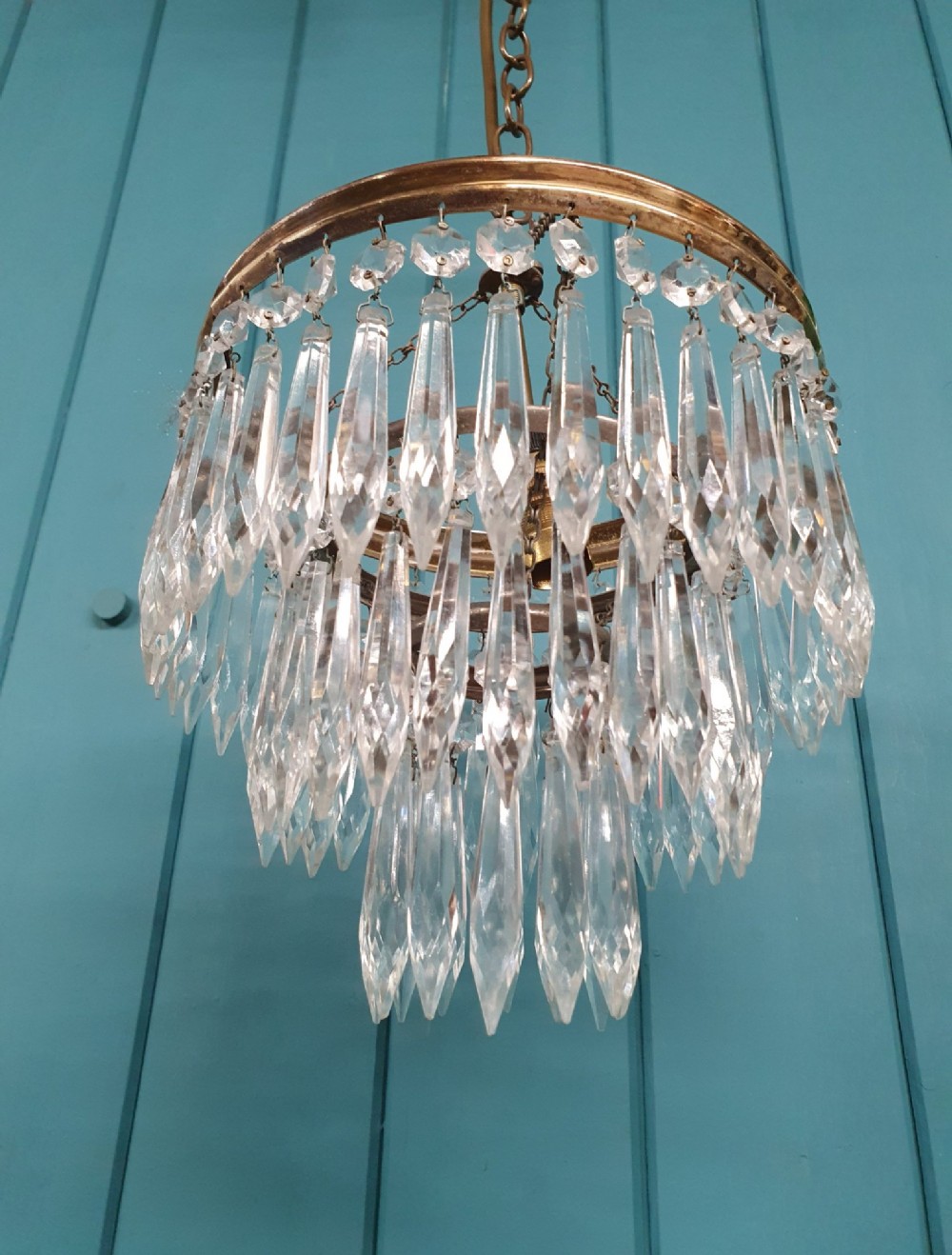 An early 20th-century brass pendant chandelier featuring tiered rings of faceted clear crystal glass spikes suspended from a chain. View III
