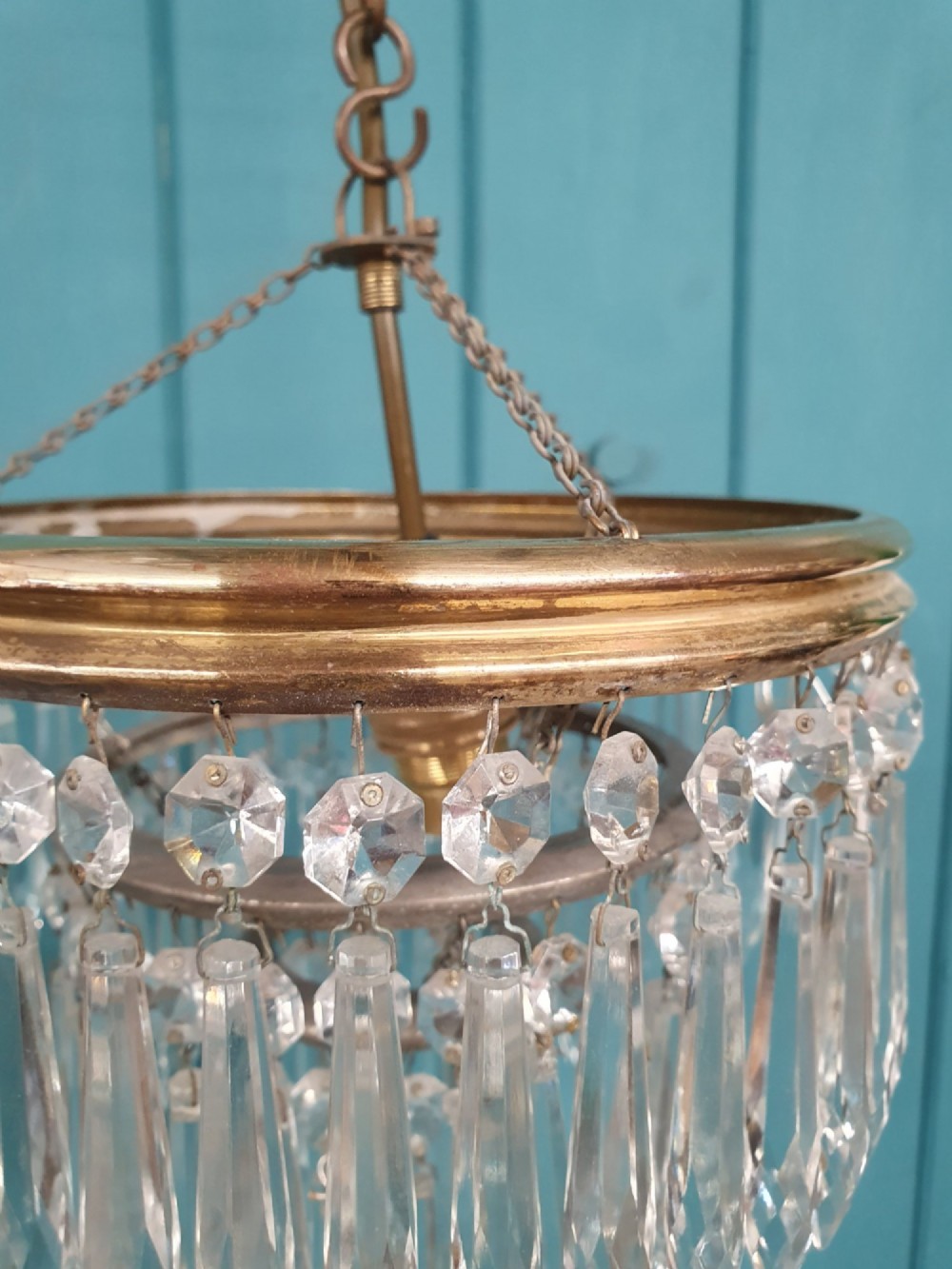 An early 20th-century brass pendant chandelier featuring tiered rings of faceted clear crystal glass spikes suspended from a chain. View IV