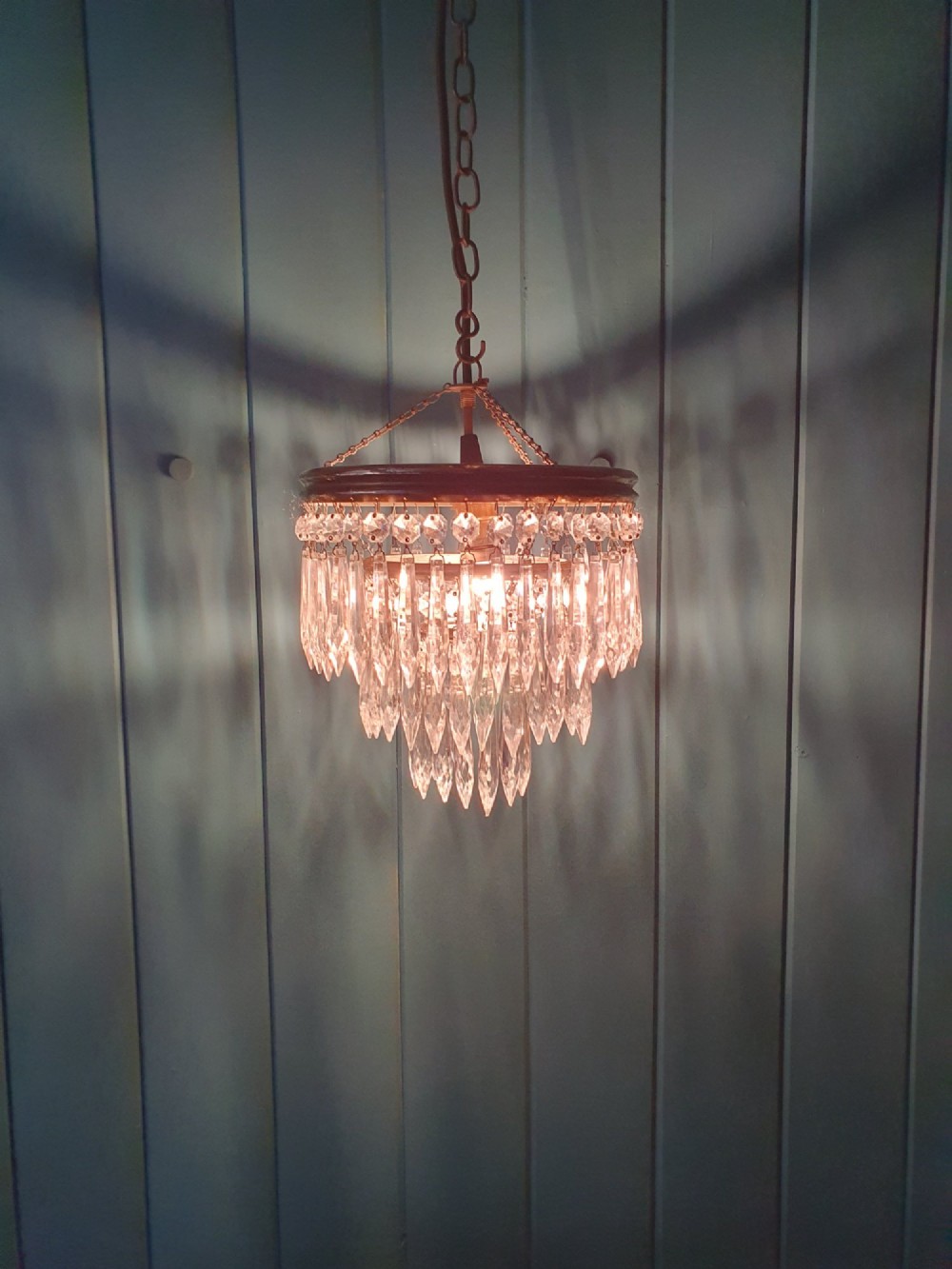 An early 20th-century brass pendant chandelier featuring tiered rings of faceted clear crystal glass spikes suspended from a chain. View V