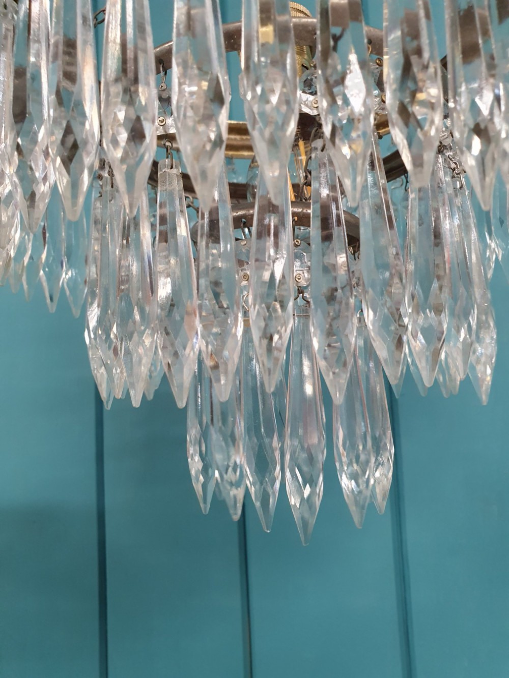 An early 20th-century brass pendant chandelier featuring tiered rings of faceted clear crystal glass spikes suspended from a chain. View VI