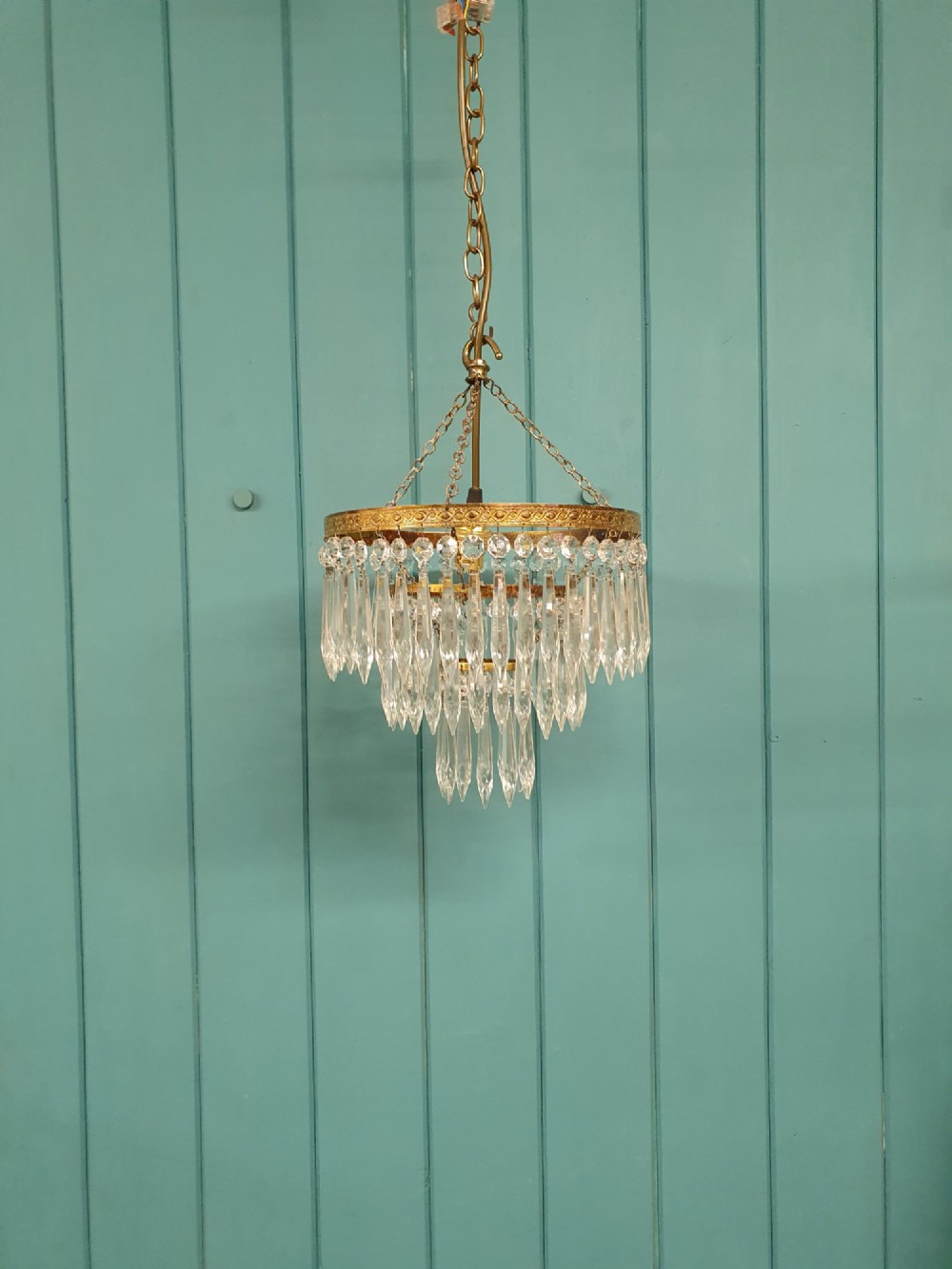 An early 20th-century brass ceiling pendant chandelier featuring three cascading tiers of clear glass spike prisms suspended from a decorative brass ring.