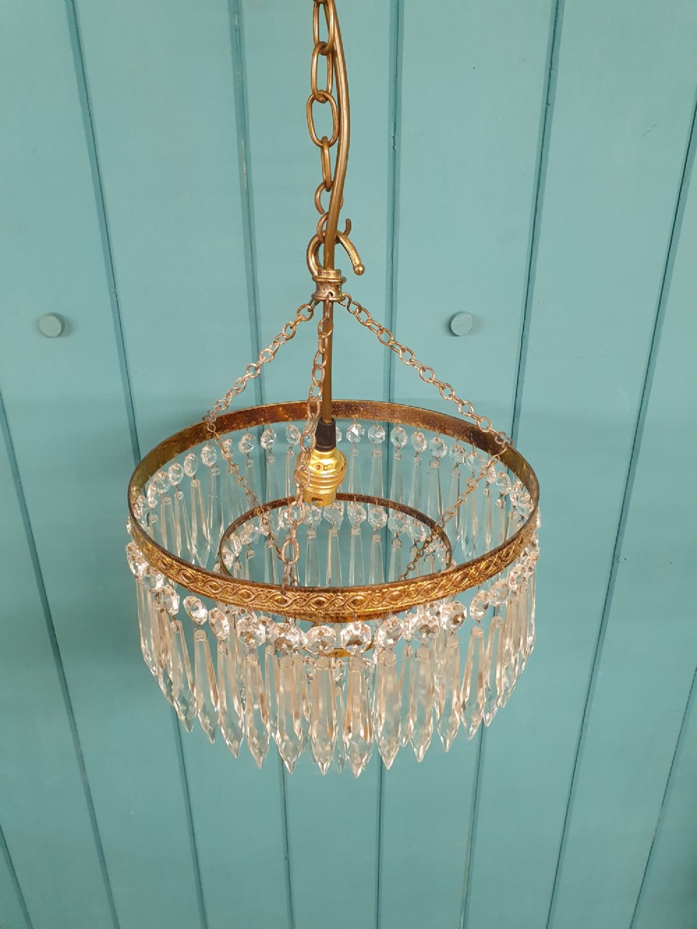An early 20th-century brass ceiling pendant chandelier featuring three cascading tiers of clear glass spike prisms suspended from a decorative brass ring. View II