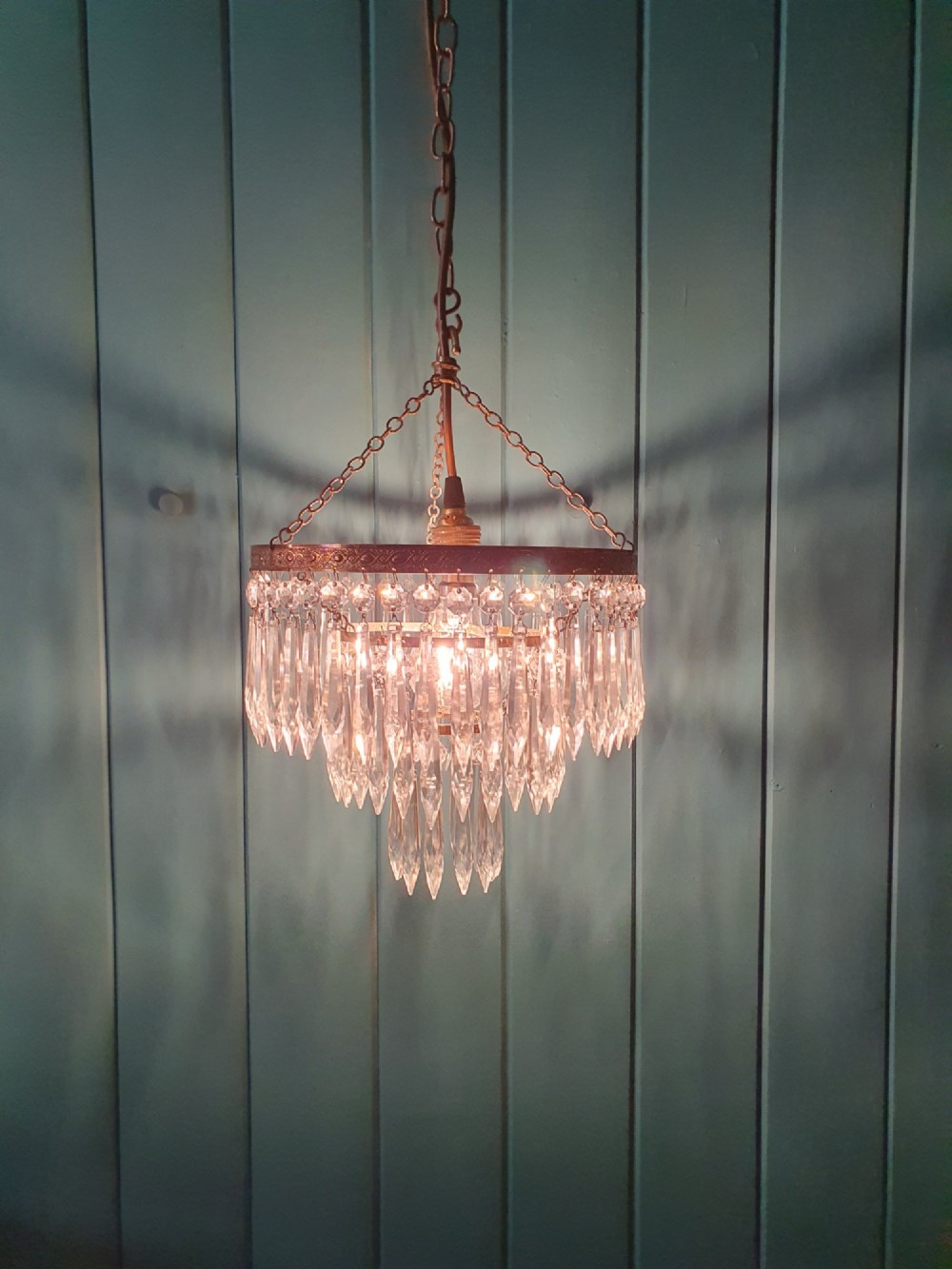 An early 20th-century brass ceiling pendant chandelier featuring three cascading tiers of clear glass spike prisms suspended from a decorative brass ring. View III