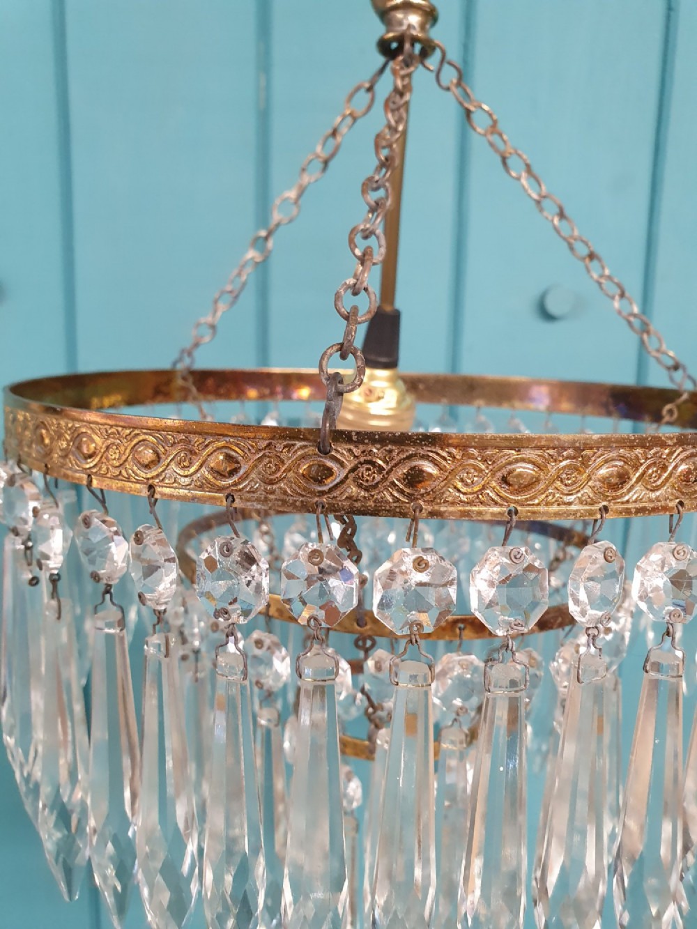 An early 20th-century brass ceiling pendant chandelier featuring three cascading tiers of clear glass spike prisms suspended from a decorative brass ring. View IV