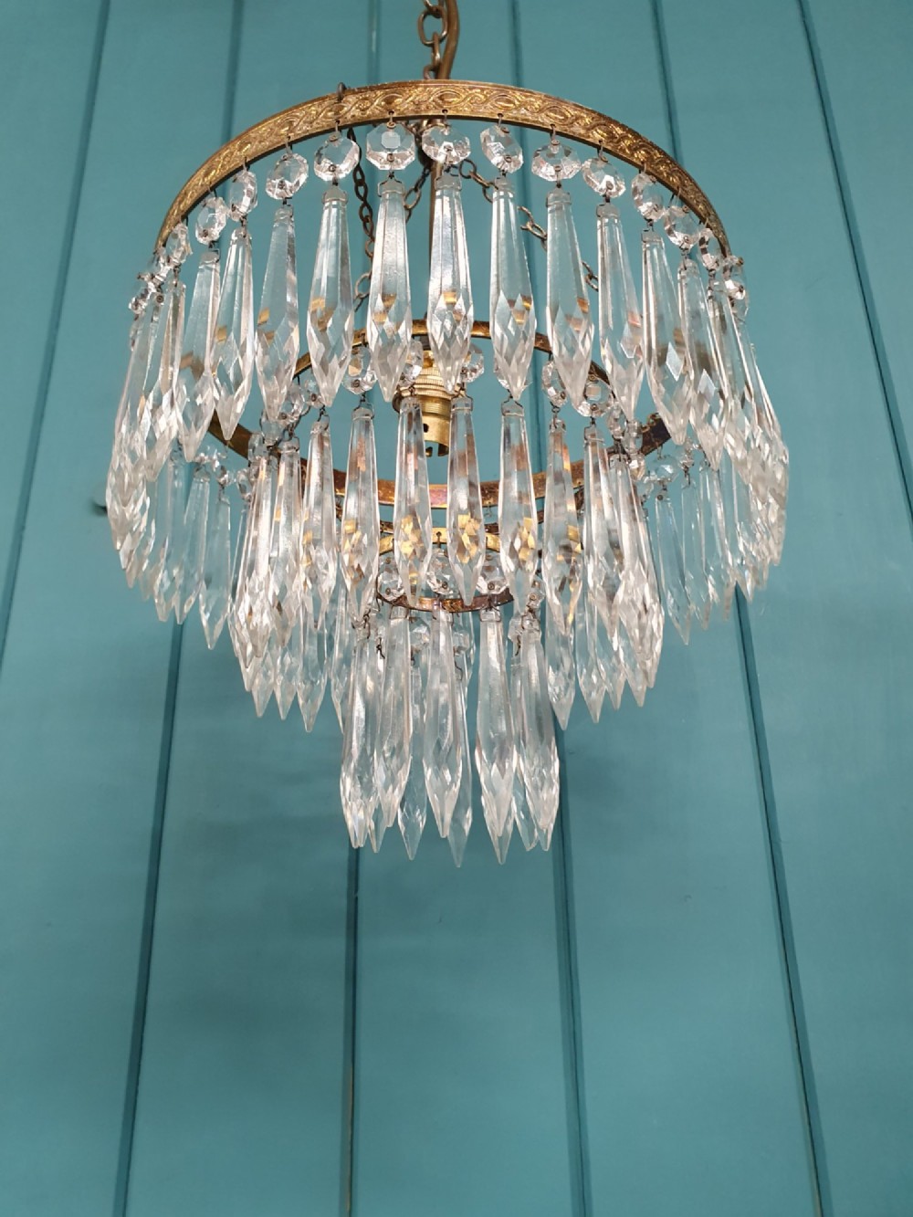 An early 20th-century brass ceiling pendant chandelier featuring three cascading tiers of clear glass spike prisms suspended from a decorative brass ring. View V