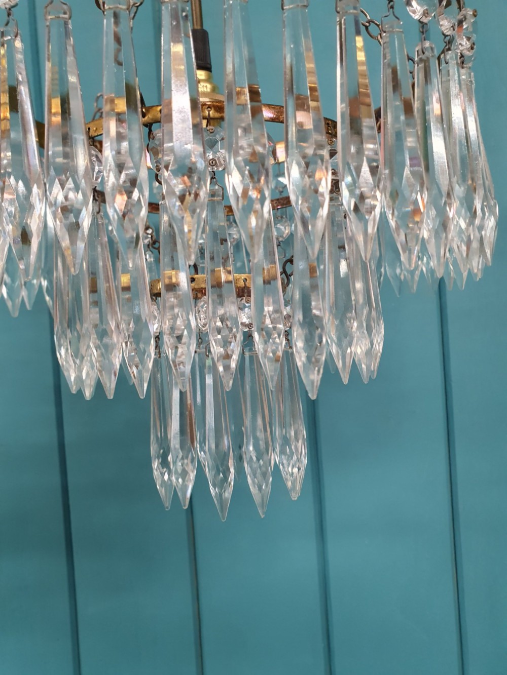 An early 20th-century brass ceiling pendant chandelier featuring three cascading tiers of clear glass spike prisms suspended from a decorative brass ring. View VI