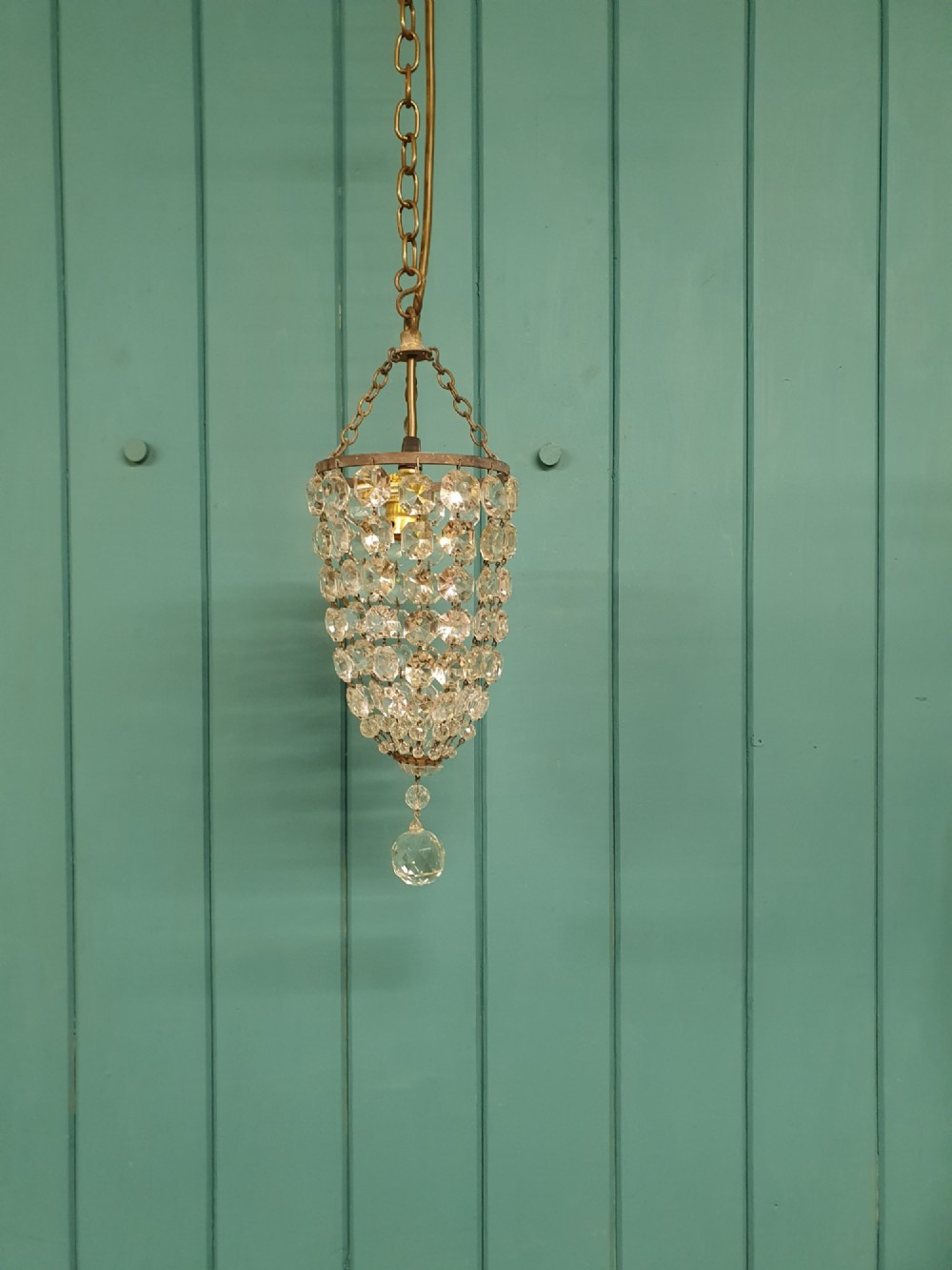 A small antique crystal bag chandelier featuring cascading faceted glass beads suspended from a circular brass frame with a chain.