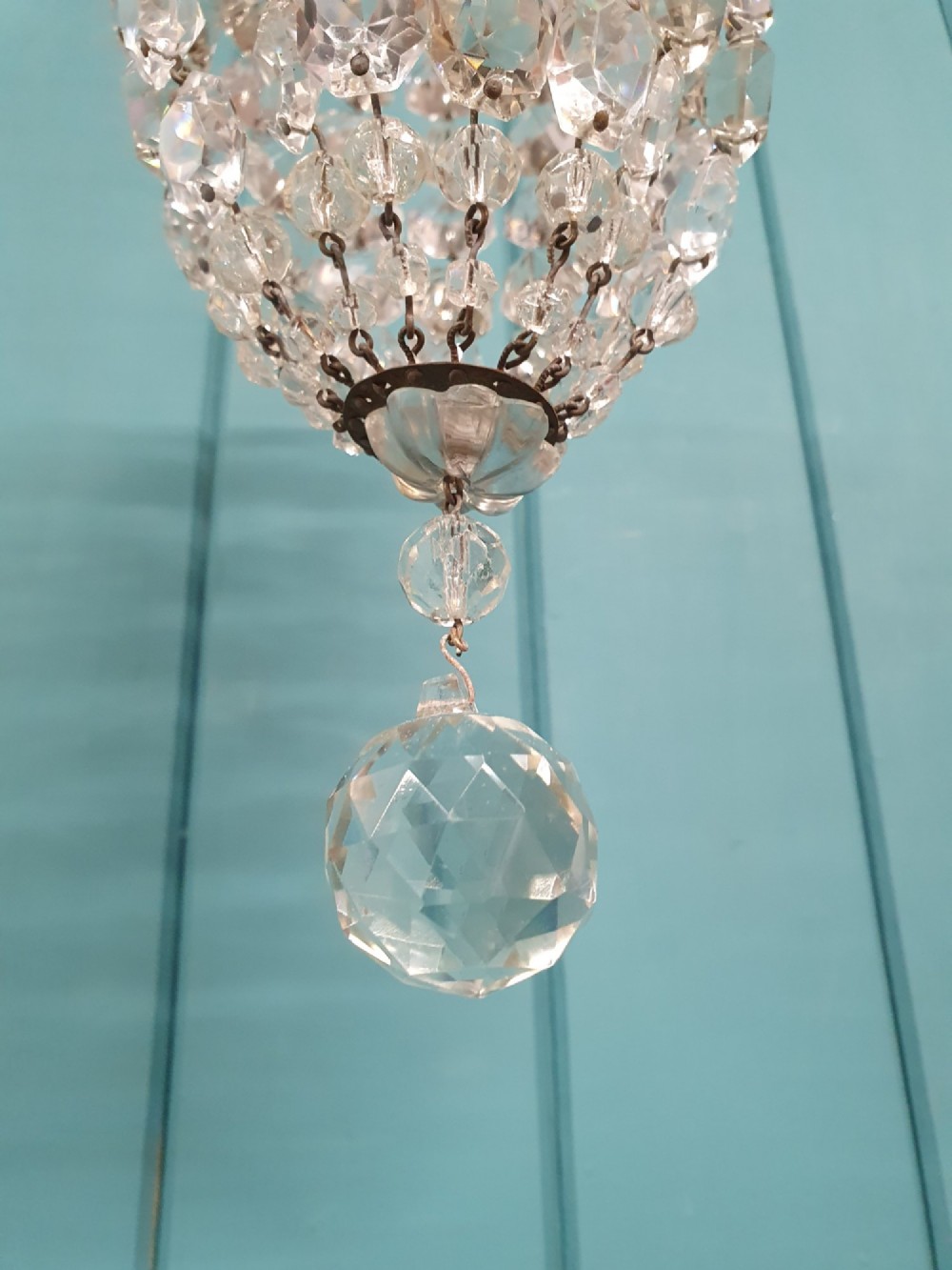 A small antique crystal bag chandelier featuring cascading faceted glass beads suspended from a circular brass frame with a chain. View V