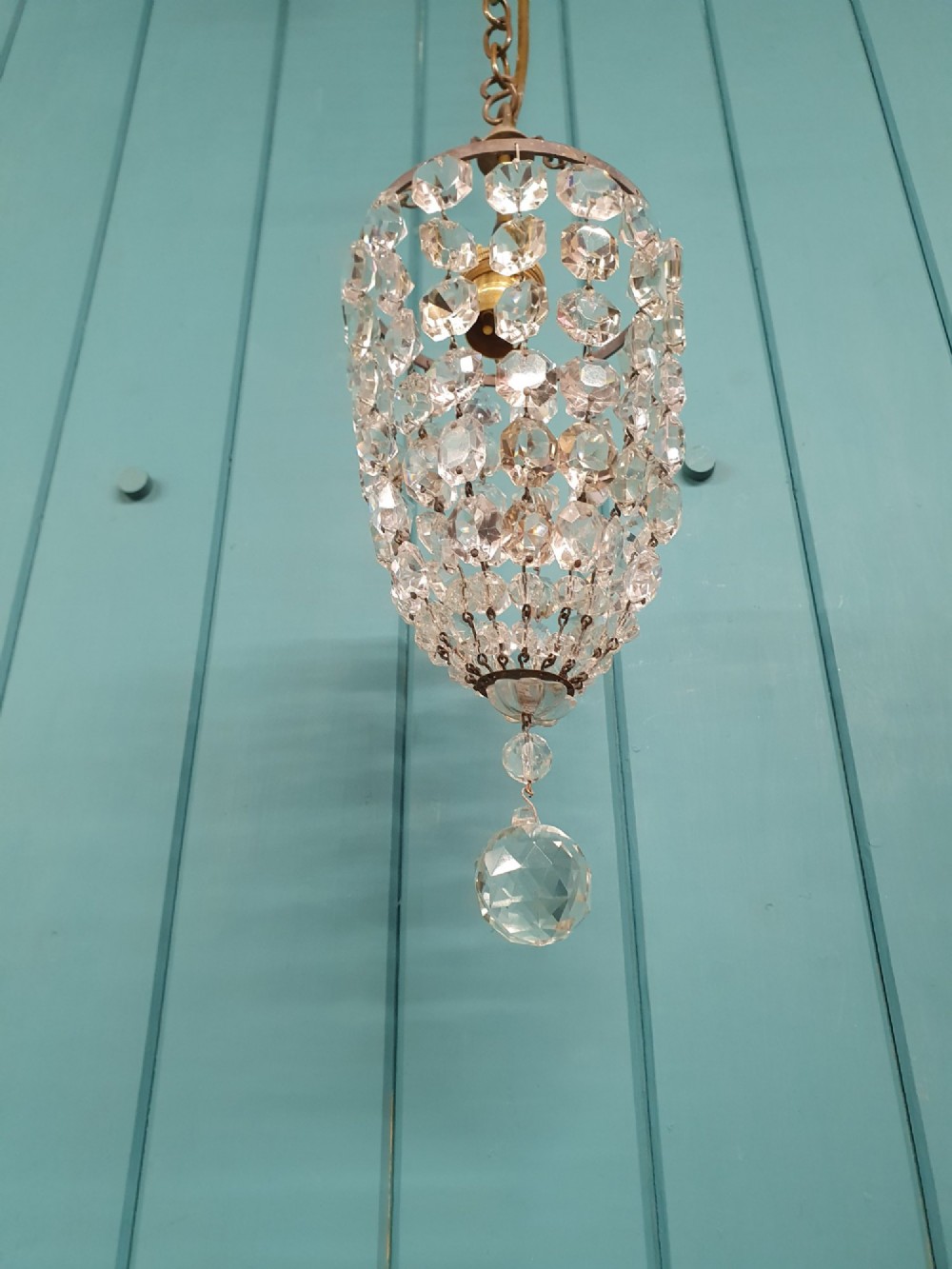 A small antique crystal bag chandelier featuring cascading faceted glass beads suspended from a circular brass frame with a chain. View VI