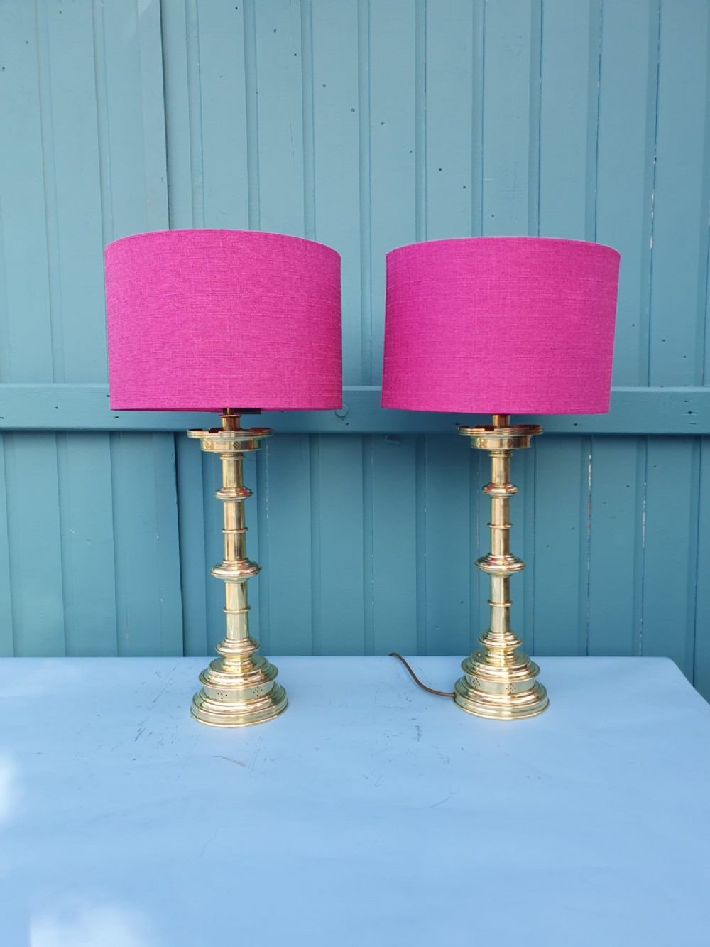 A pair of turned brass column table lamps topped with cylindrical bright pink fabric shades.