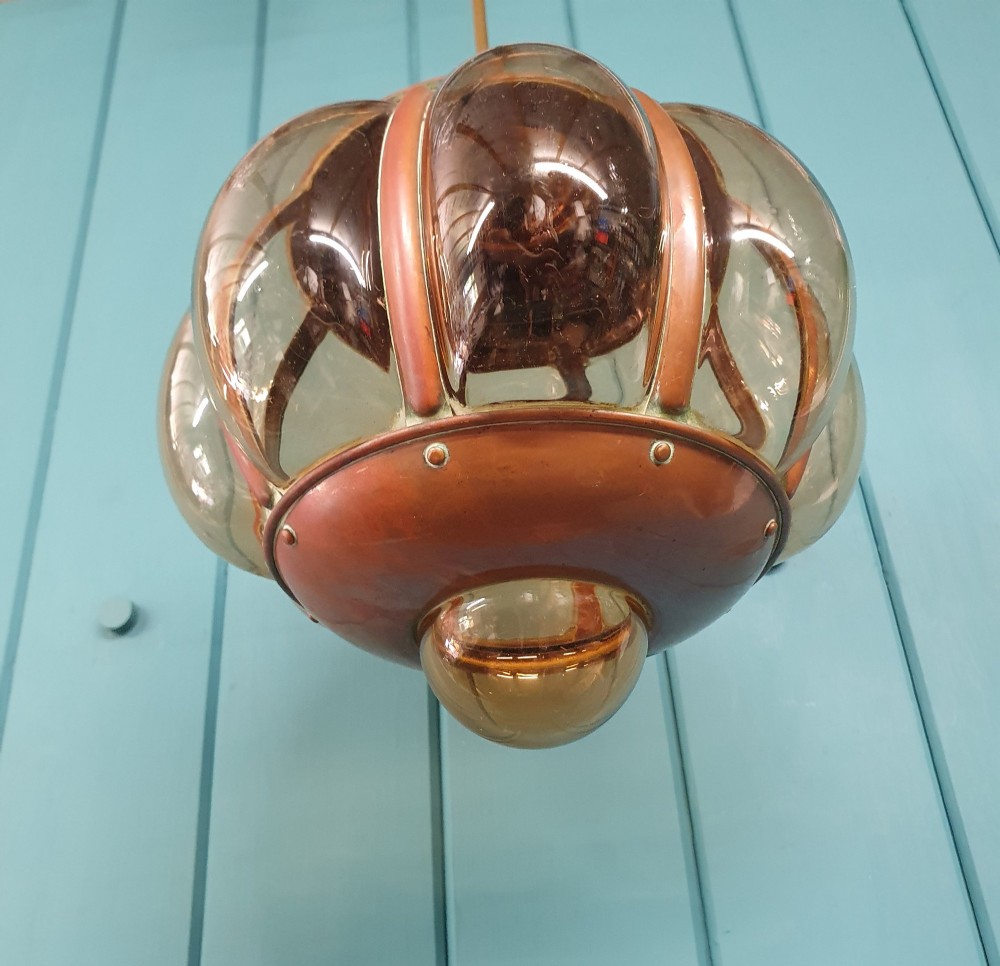 A spherical nautical pendant light featuring a copper cap and framed body enclosing a ribbed smoked amber glass globe. View II
